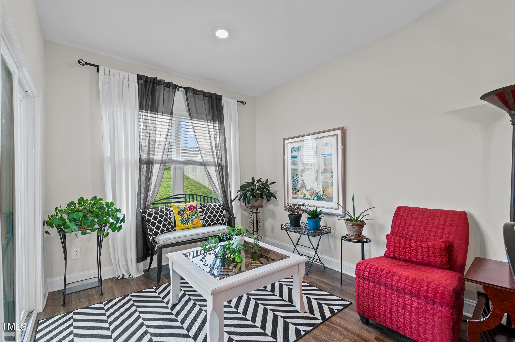 Sitting room with a curtained window, red armchair, potted plants, and chevron rug.
