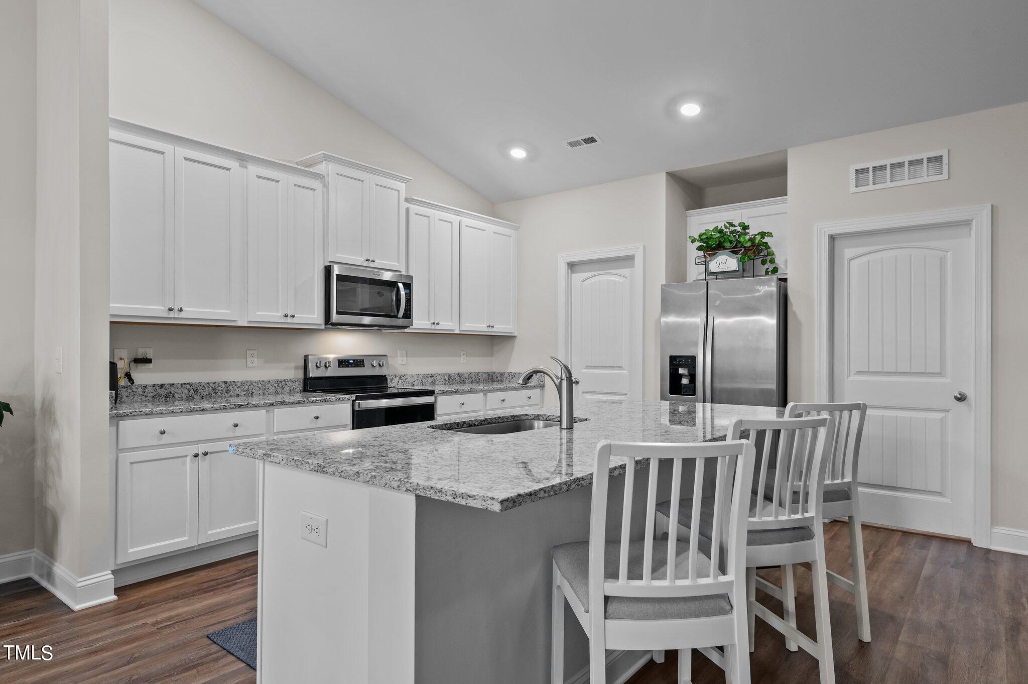 Kitchen with white cabinets, stainless appliances, granite island, and three stools.