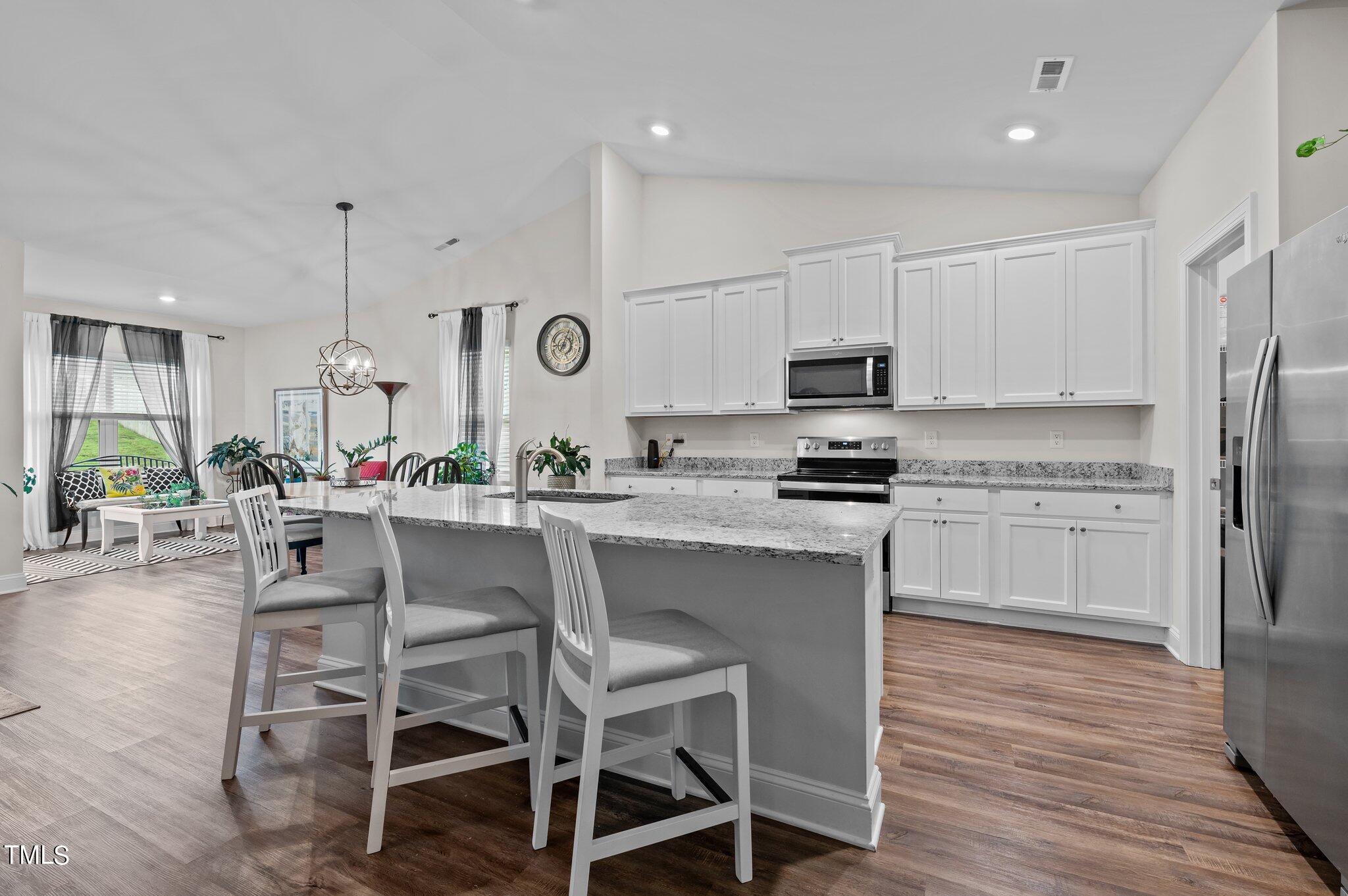 Kitchen with a large granite island, white cabinetry, and stainless steel appliances beside a sitting area.