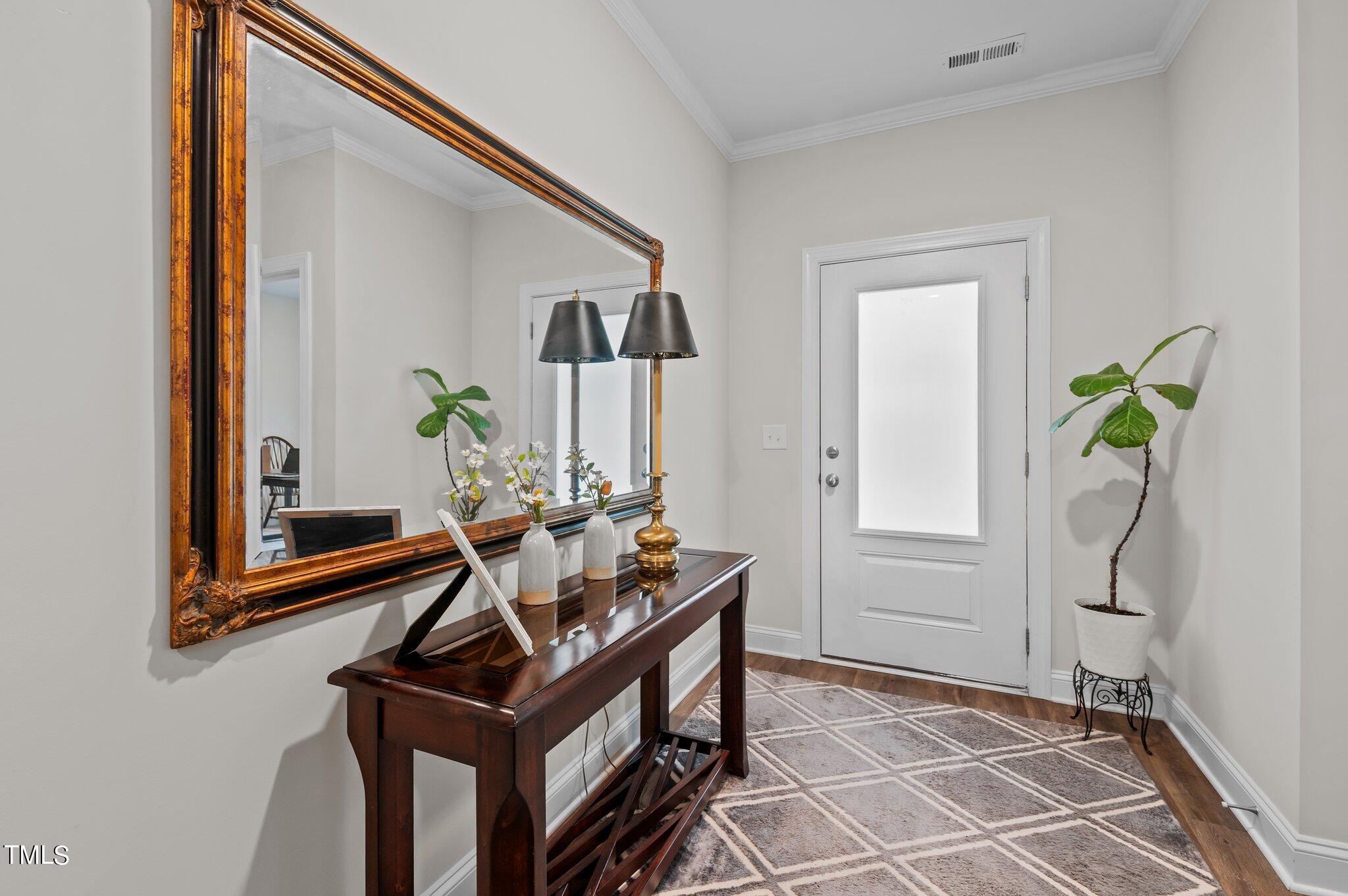 Entryway with a white front door, ornate gold-framed mirror, and dark wood console table.