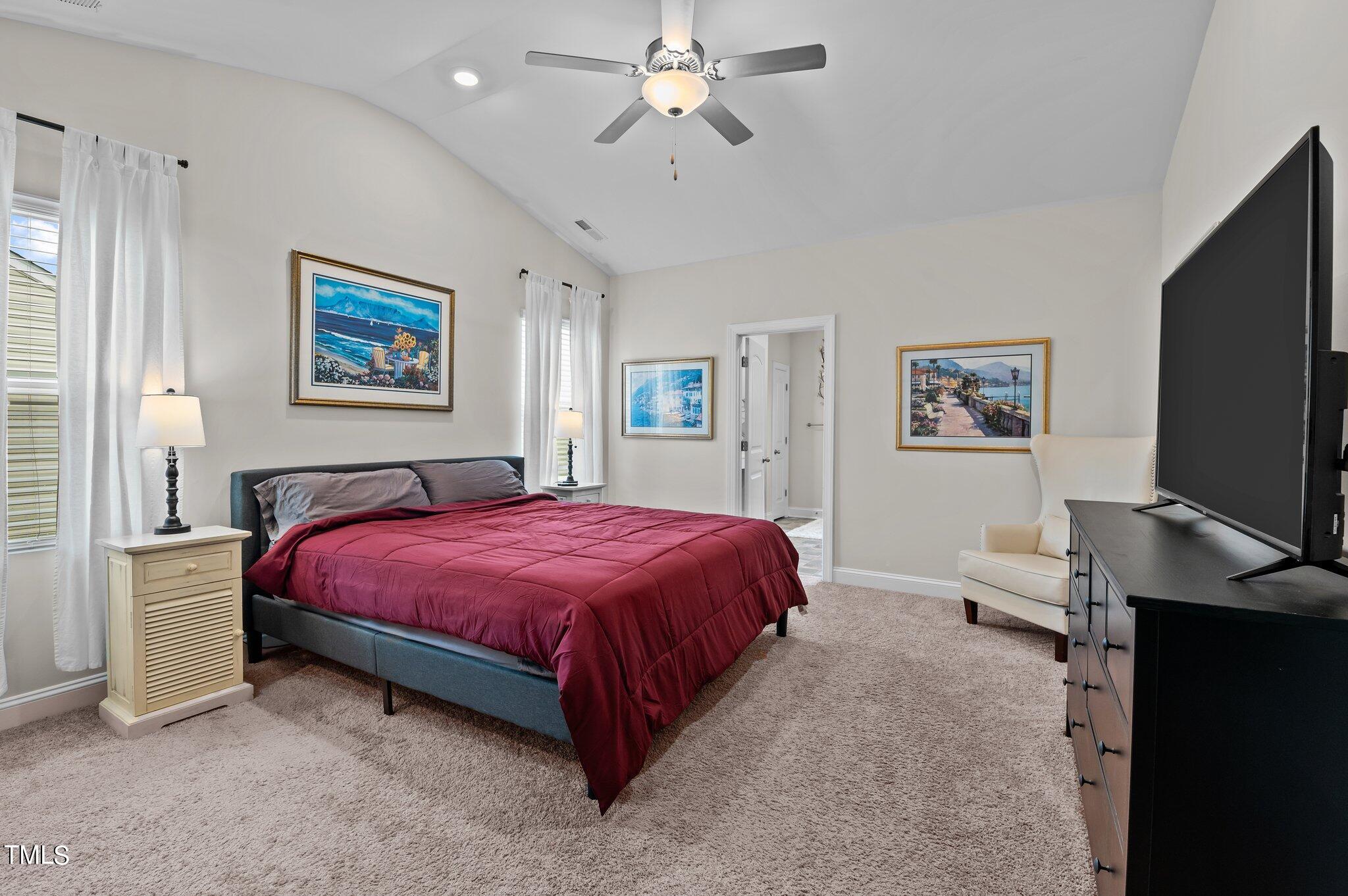 Furnished bedroom with a burgundy bedspread, vaulted ceiling, and large television beside a cream armchair.