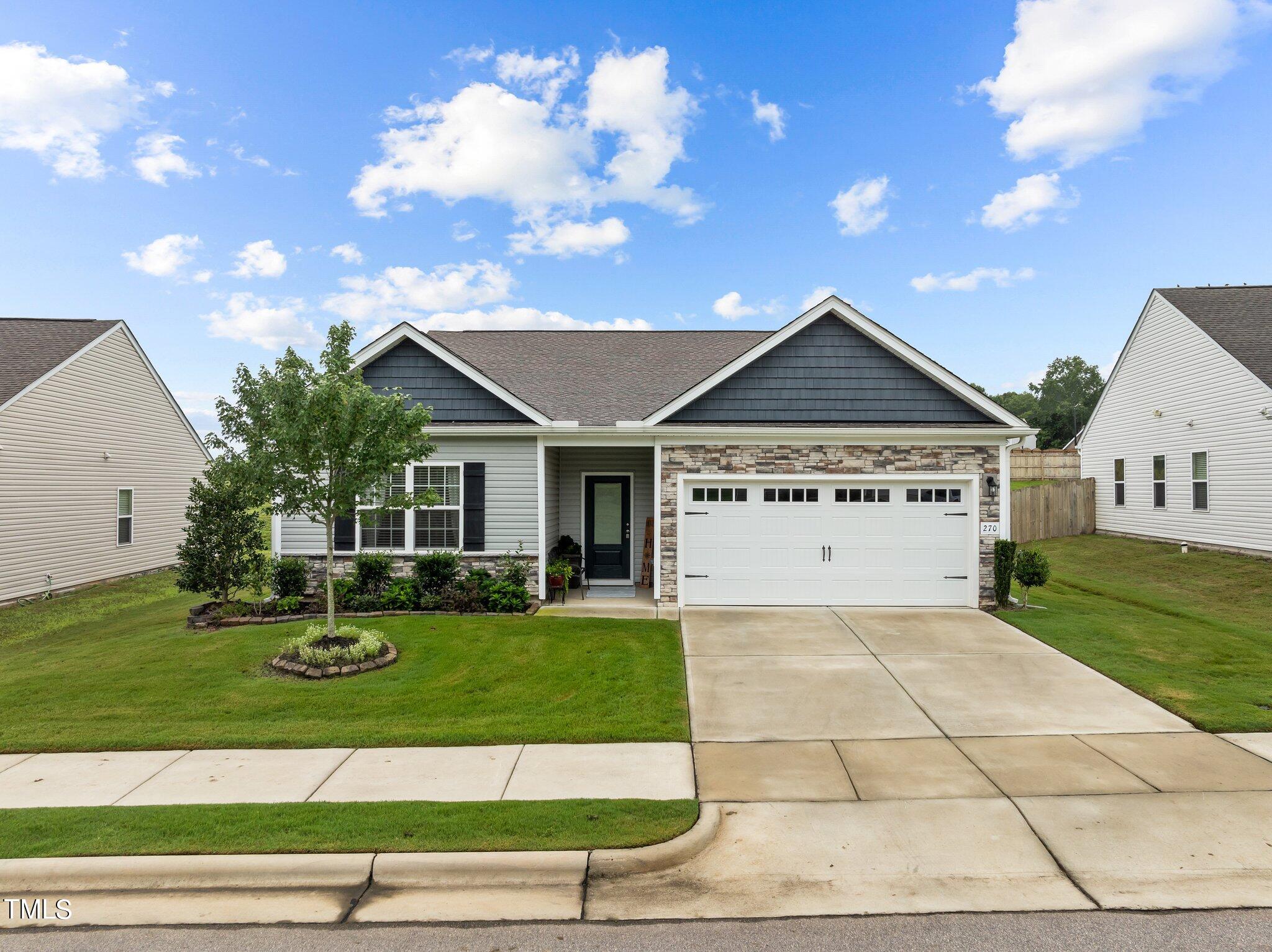 Single-story gray home with stone accents, a two-car garage, and landscaped front lawn.