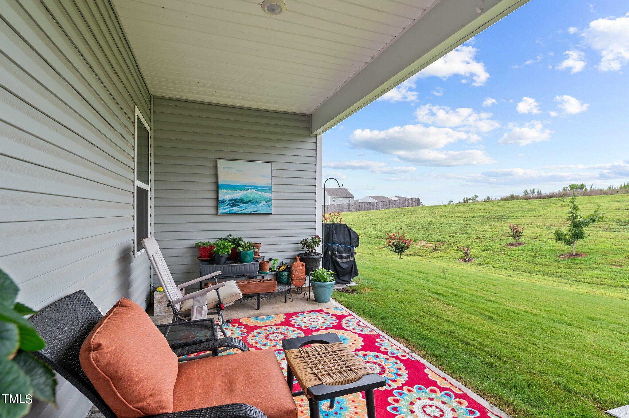 Covered patio with wicker seating and potted plants overlooking a spacious green lawn.