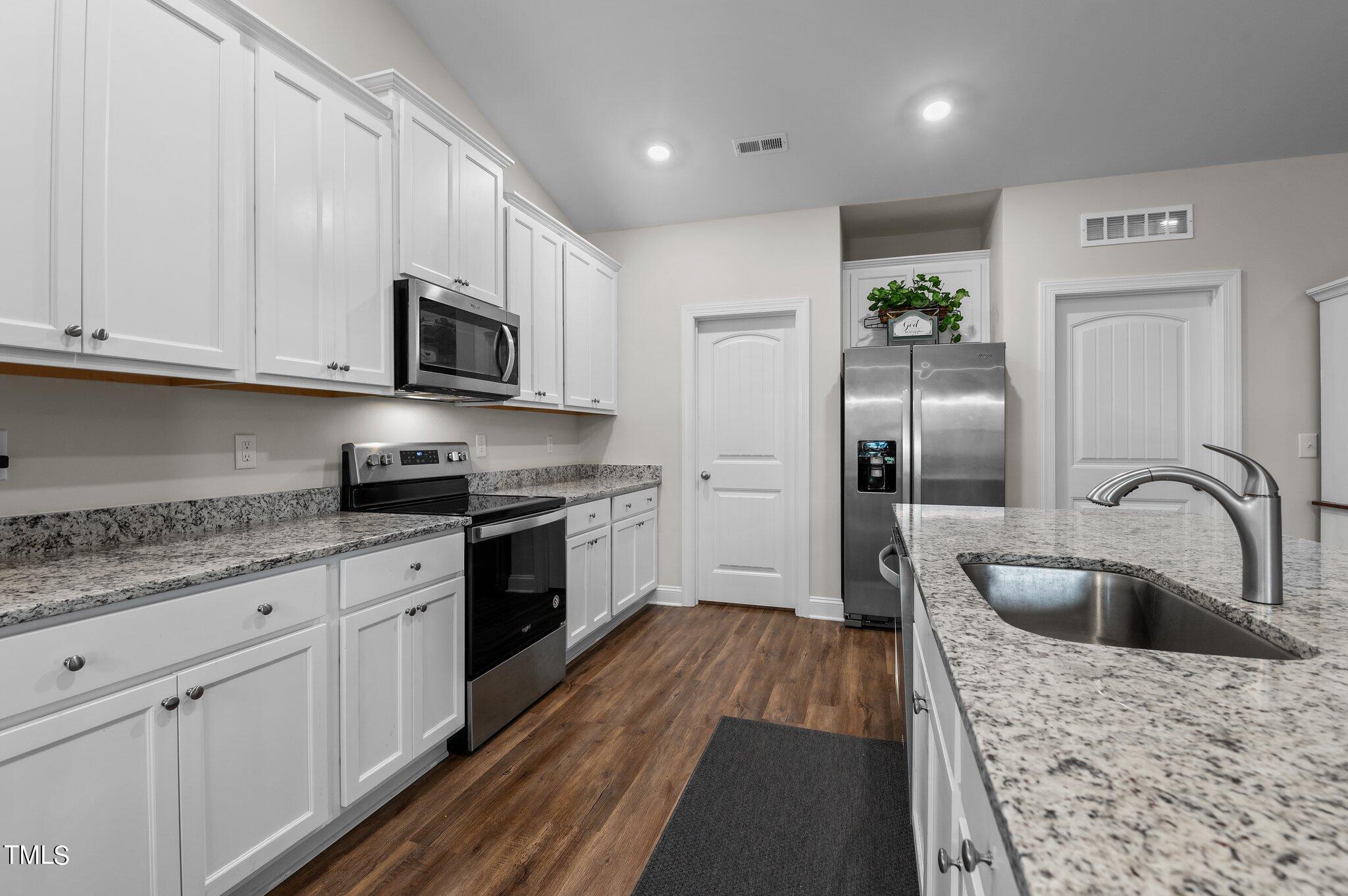 Kitchen with white cabinets, granite counters, stainless steel appliances, and a large sink island.