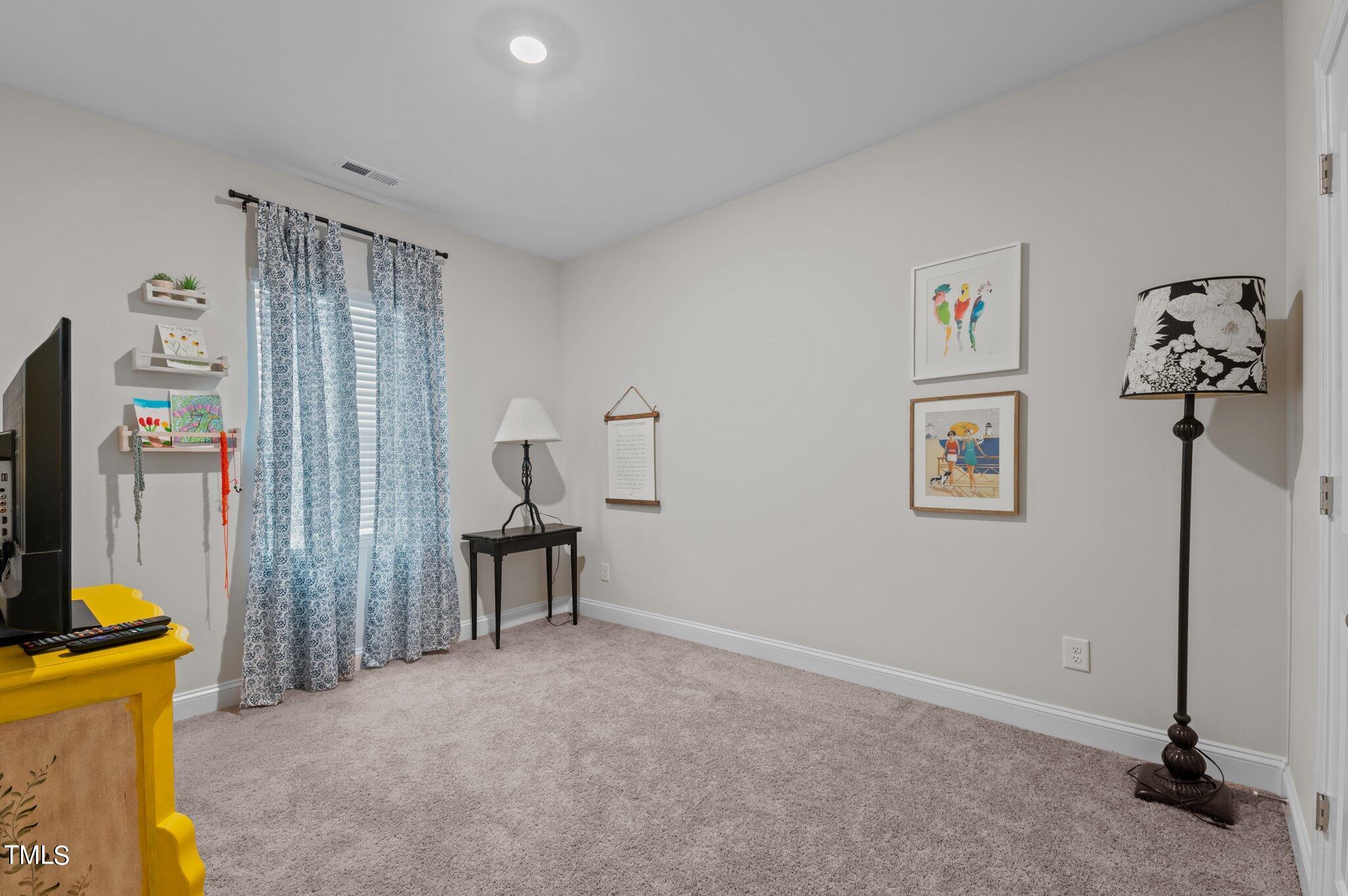 Carpeted room with blue patterned curtains, framed art, a television, and a bright yellow cabinet.