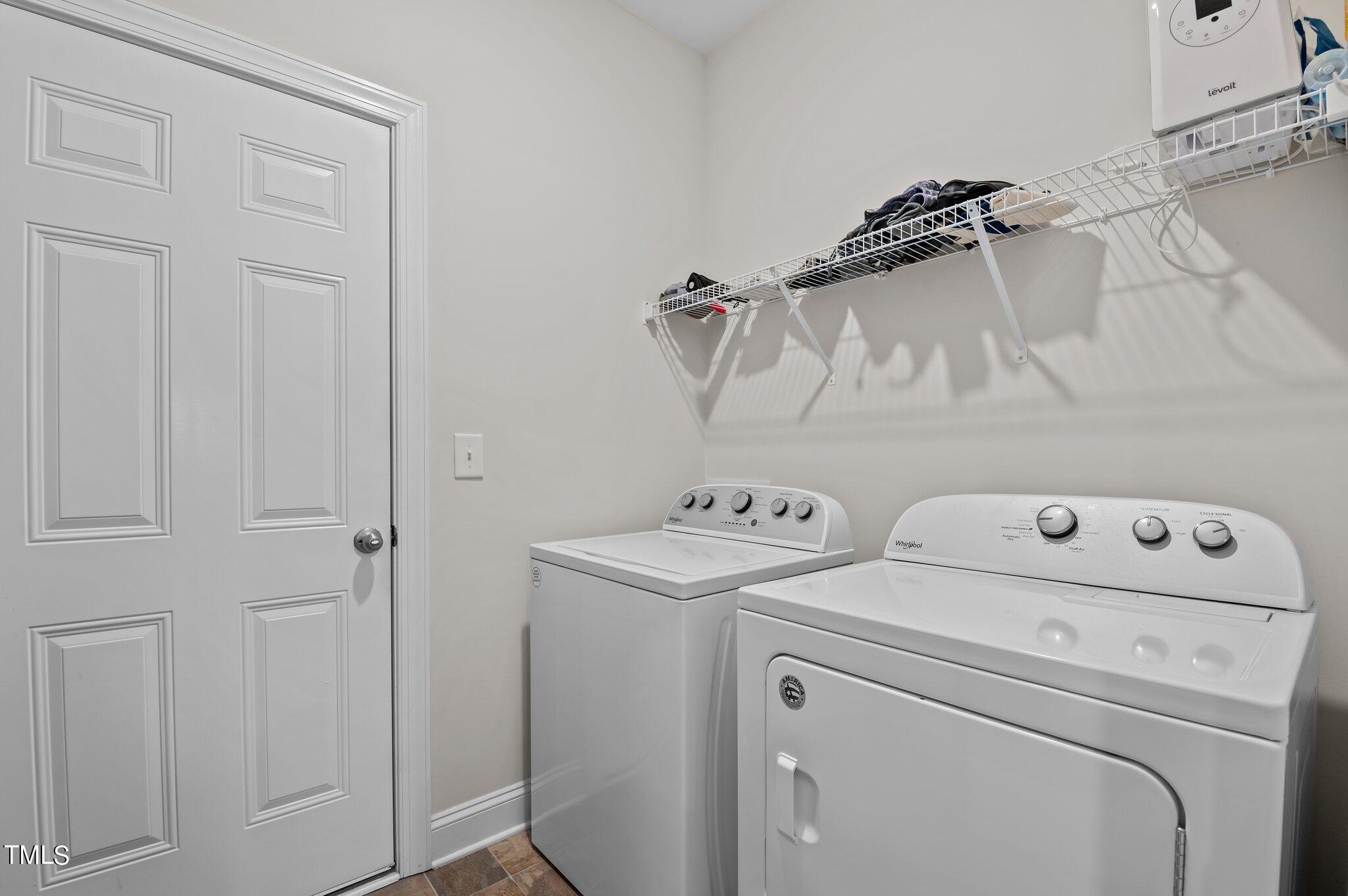 Laundry room with a white washer and dryer beneath a wire storage shelf.