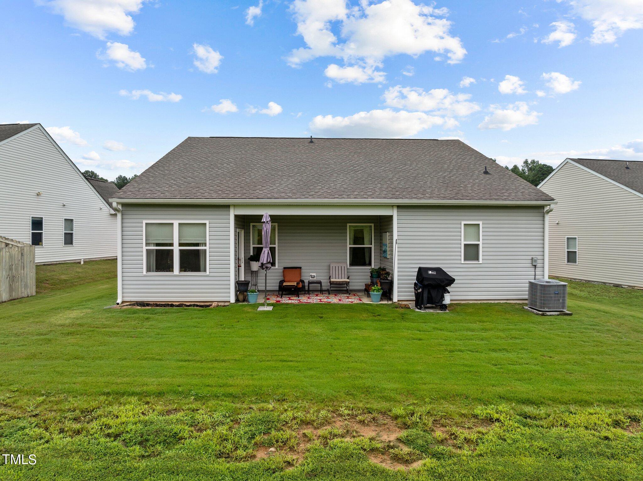 Rear of a gray-sided home with a covered furnished patio and broad grassy backyard.