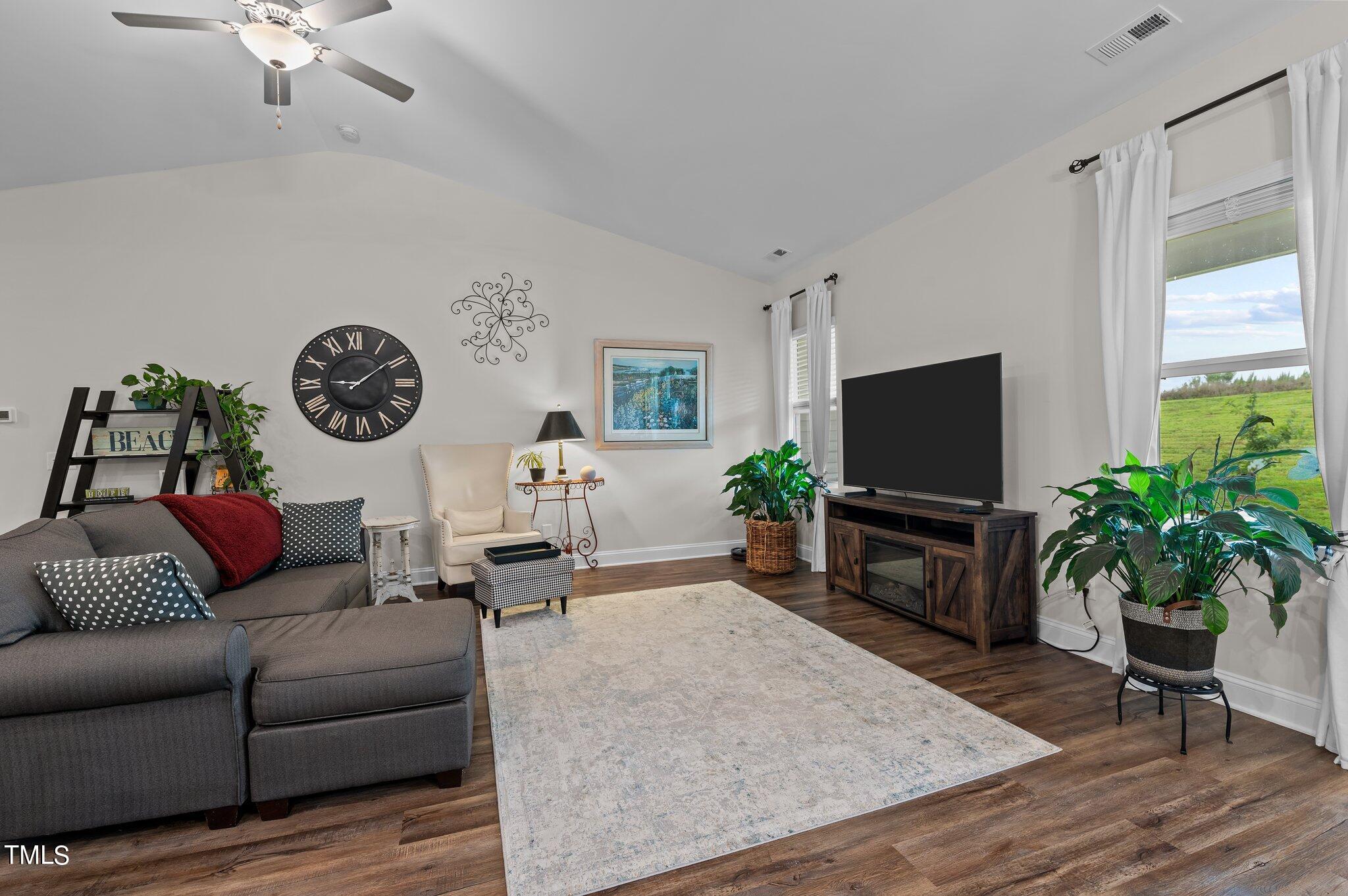 Living room with a gray sectional, television, vaulted ceiling, and windows overlooking a green field.