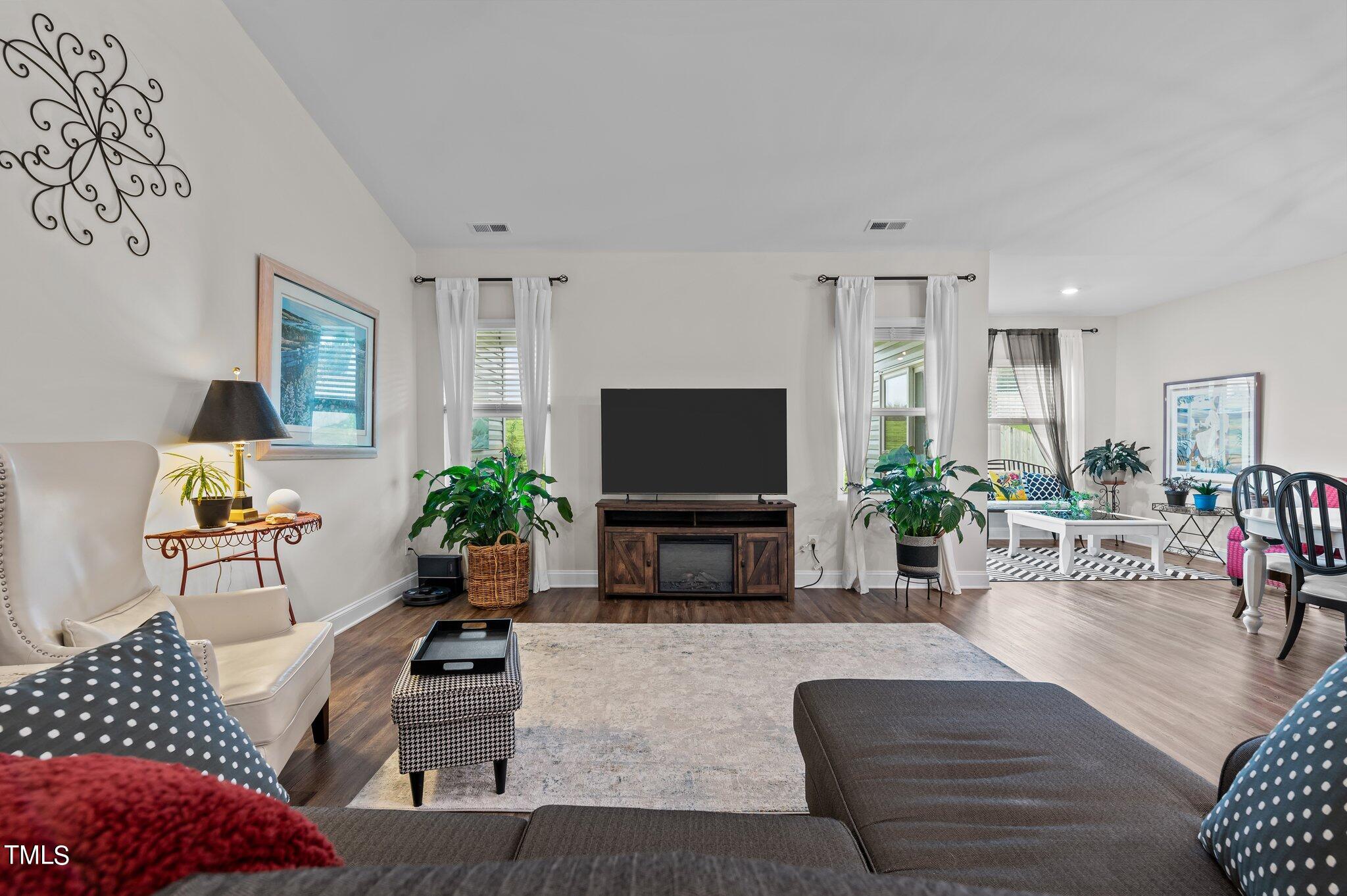 Furnished living room with a television, leafy plants, and an adjoining sitting area.