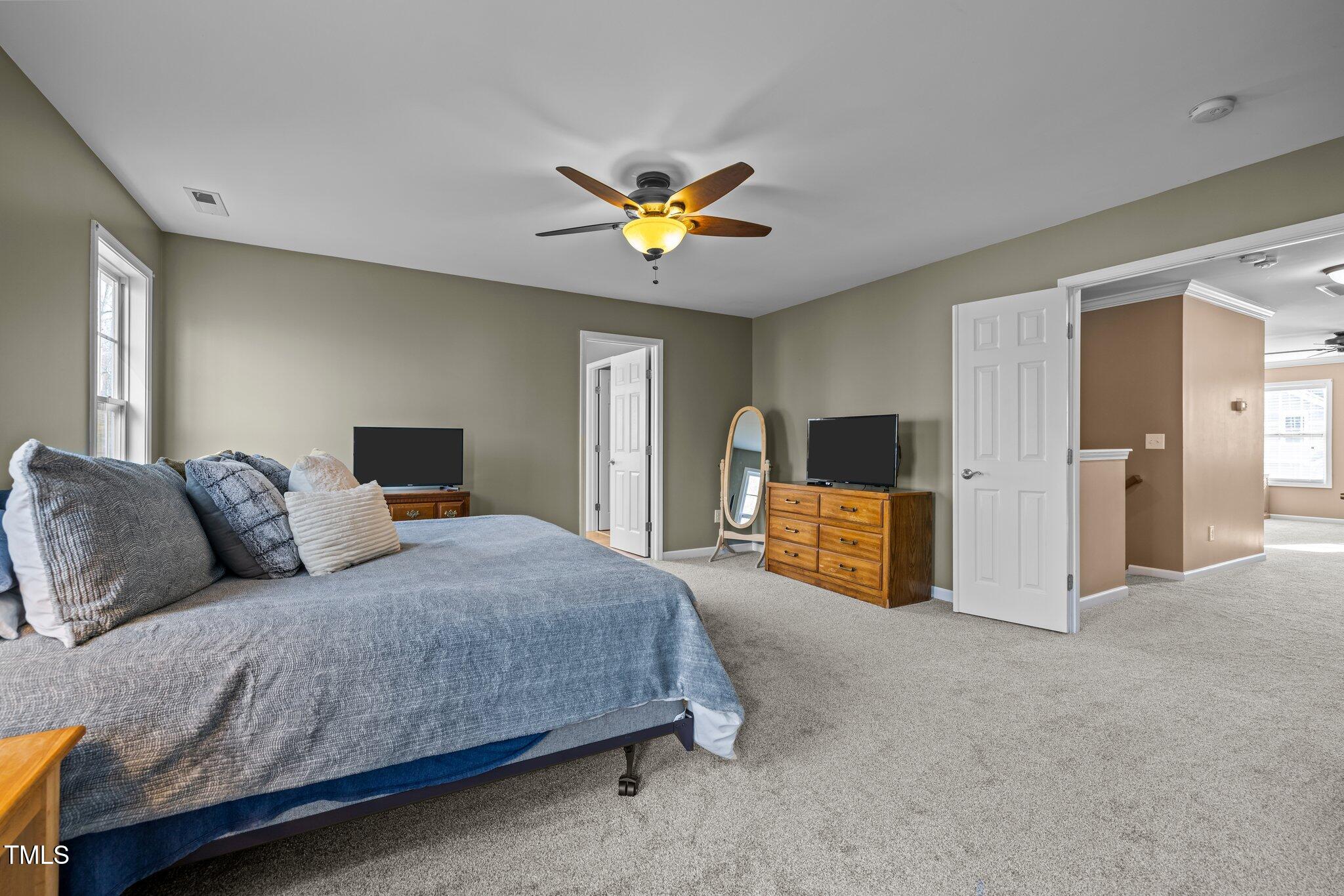 Furnished bedroom with a large blue-gray bed, ceiling fan, and wooden dressers.