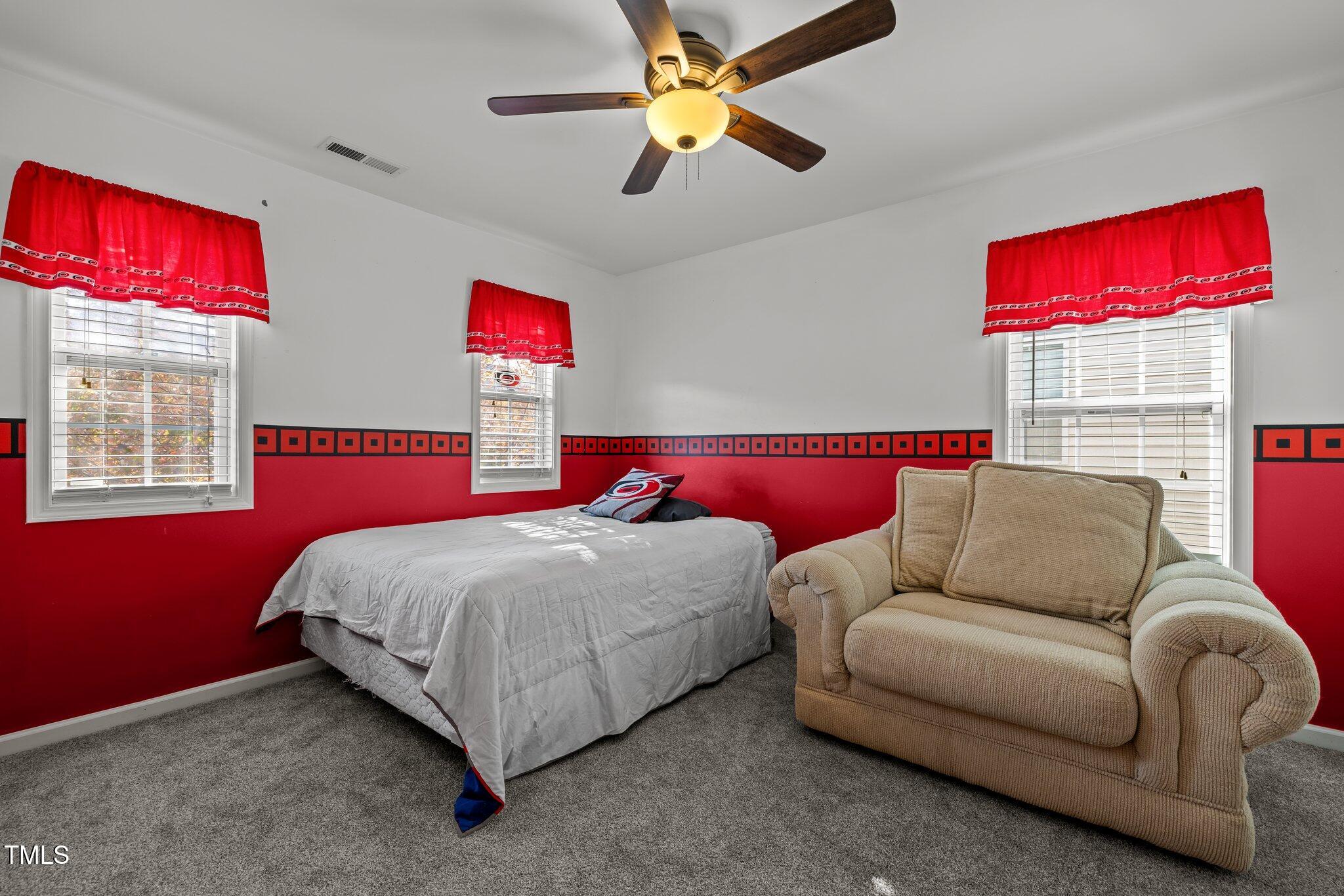 Bedroom with a bed and beige armchair, red-and-black walls, and three windows with red valances.