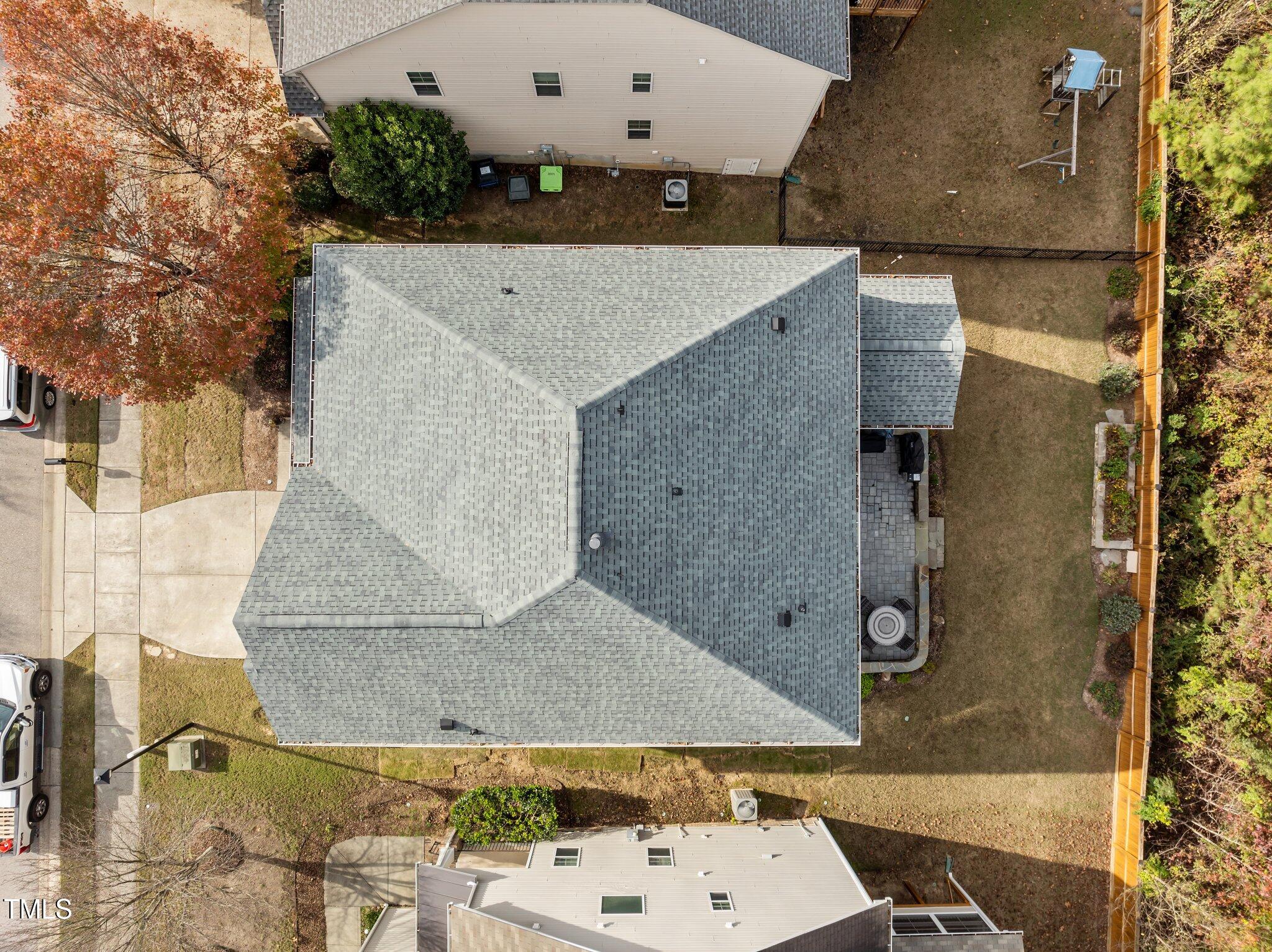 Aerial view of a gray-roofed home, fenced backyard, and patio.