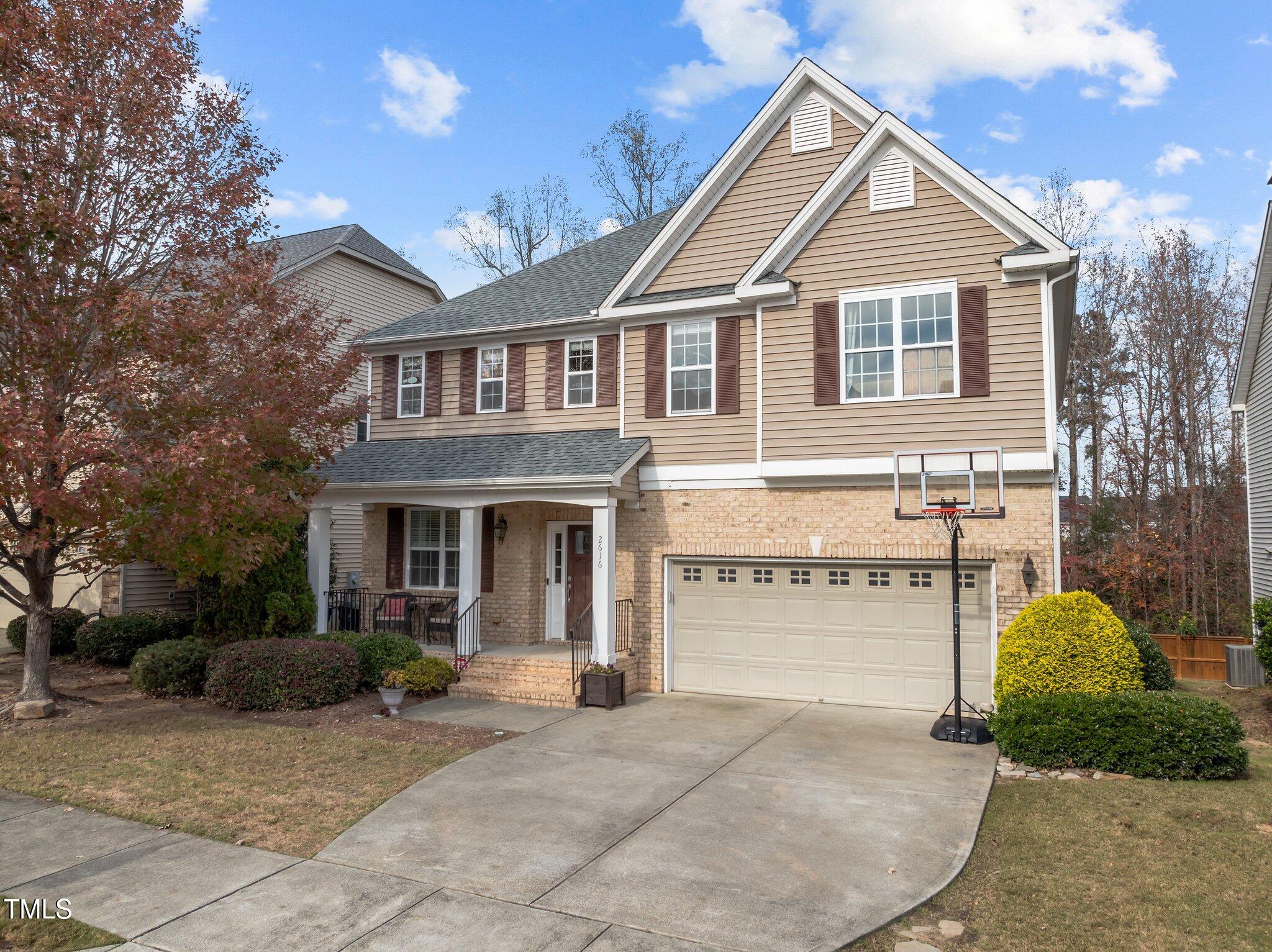 Two-story tan-and-brick home with a covered porch, double garage, and basketball hoop in the driveway.
