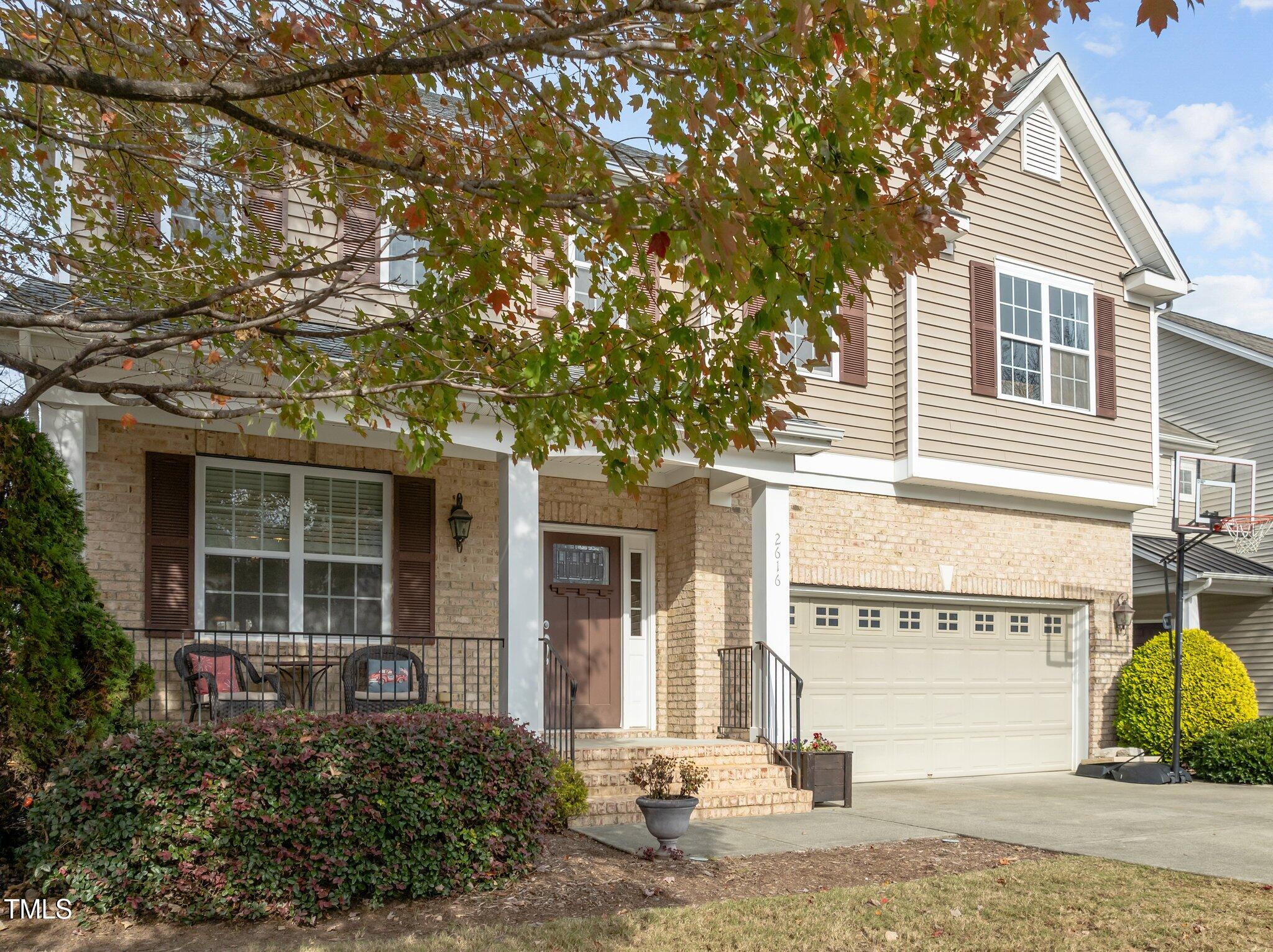 Two-story brick-and-siding home with a covered porch, double garage, and basketball hoop.