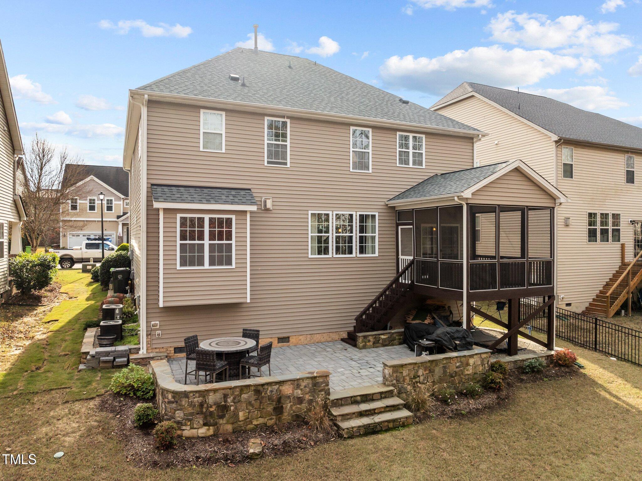 Rear of a two-story home with a raised screened porch and stone-edged patio.