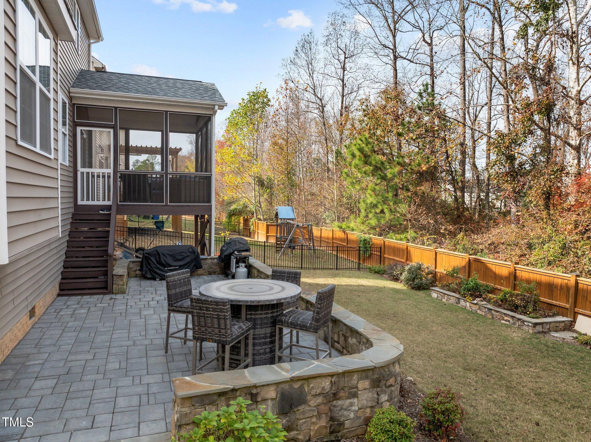 Backyard patio with round dining table, curved stone wall, and raised screened porch.