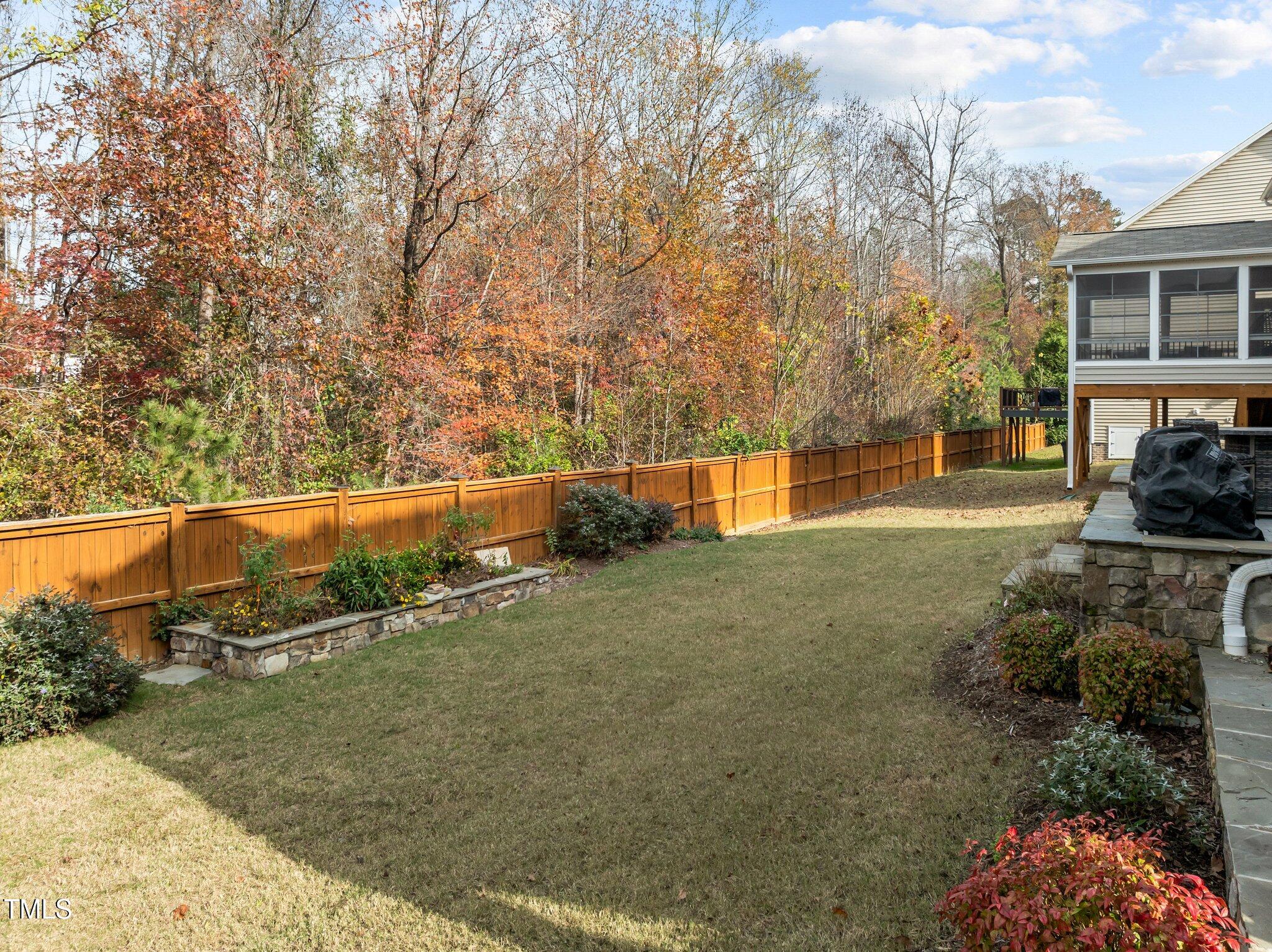 Backyard with a broad lawn, wooden privacy fence, stone planting beds, and raised screened porch.