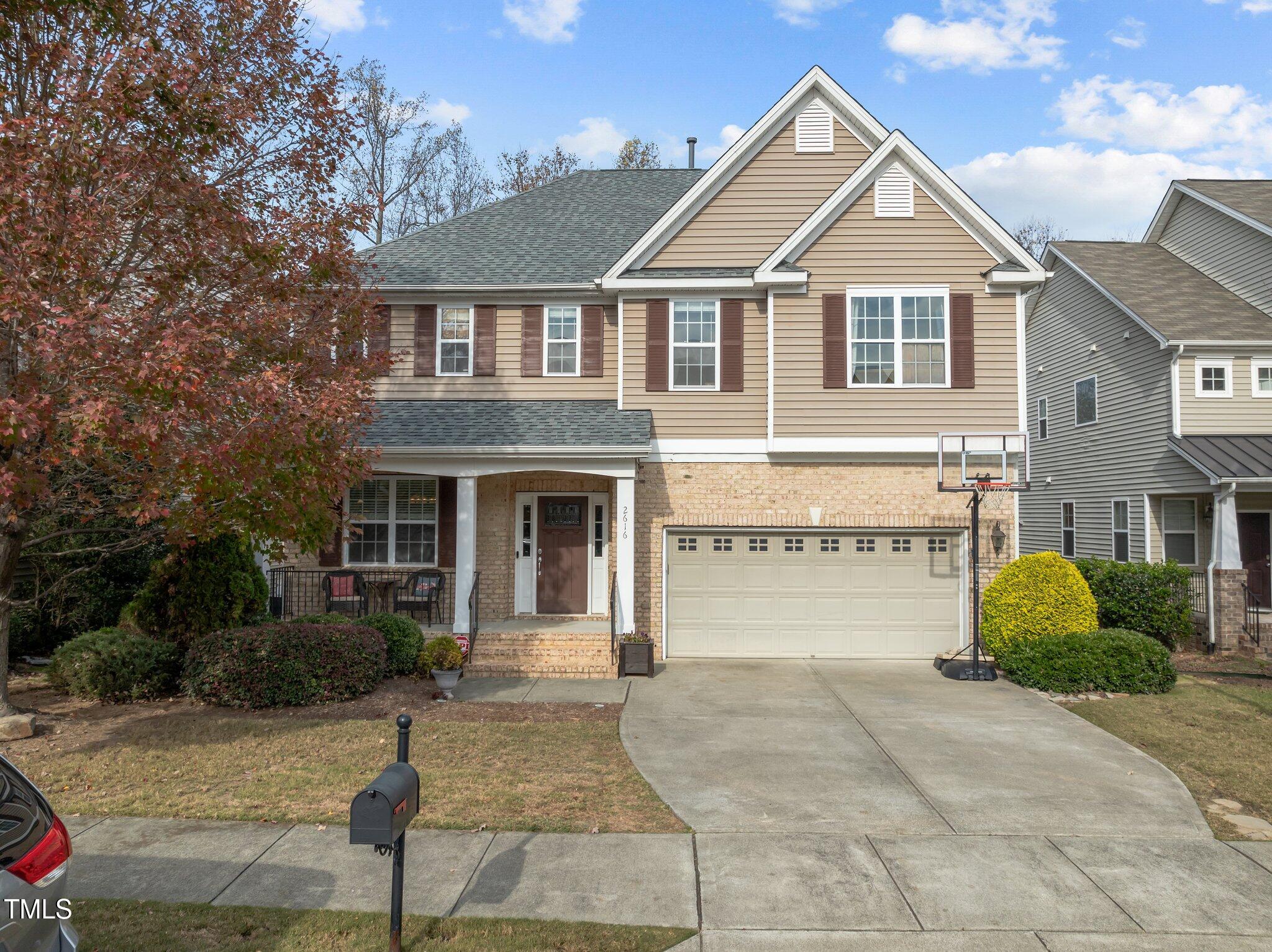Two-story tan house with brick accents, twin gables, a double garage, and a basketball hoop by the driveway.