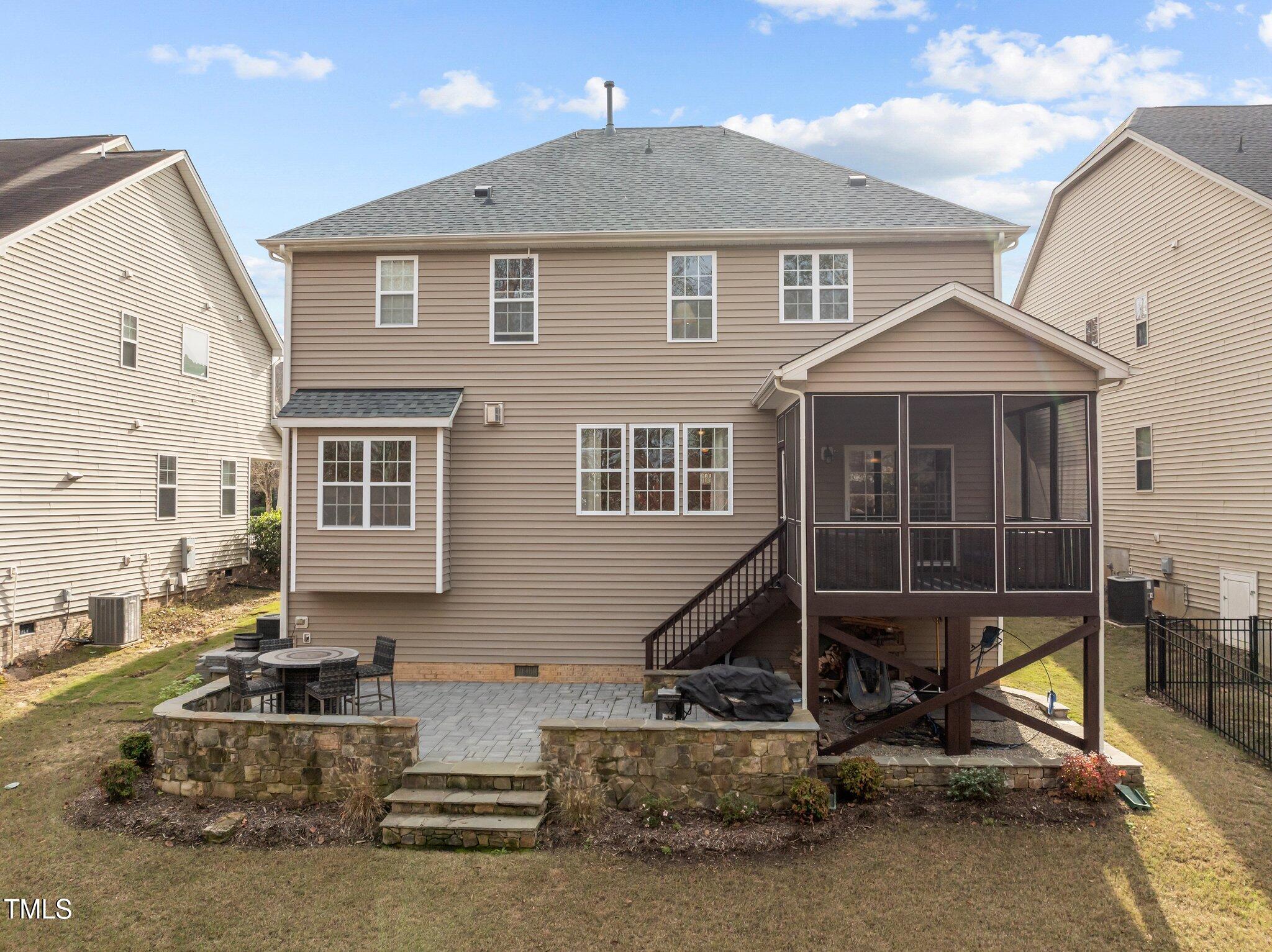 Rear of a two-story house with a raised screened porch and stone-edged patio.