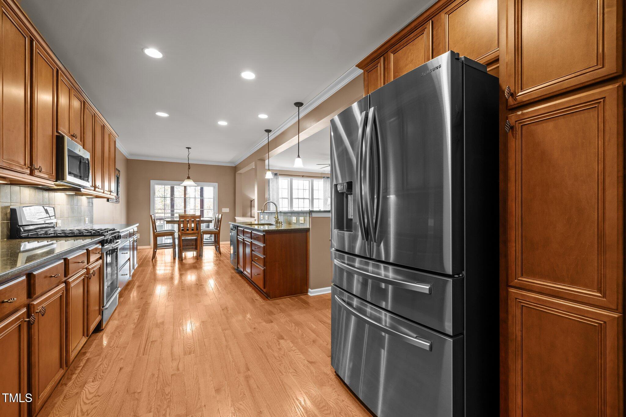 Kitchen with warm wood cabinetry, hardwood floors, stainless steel appliances, and a central island.