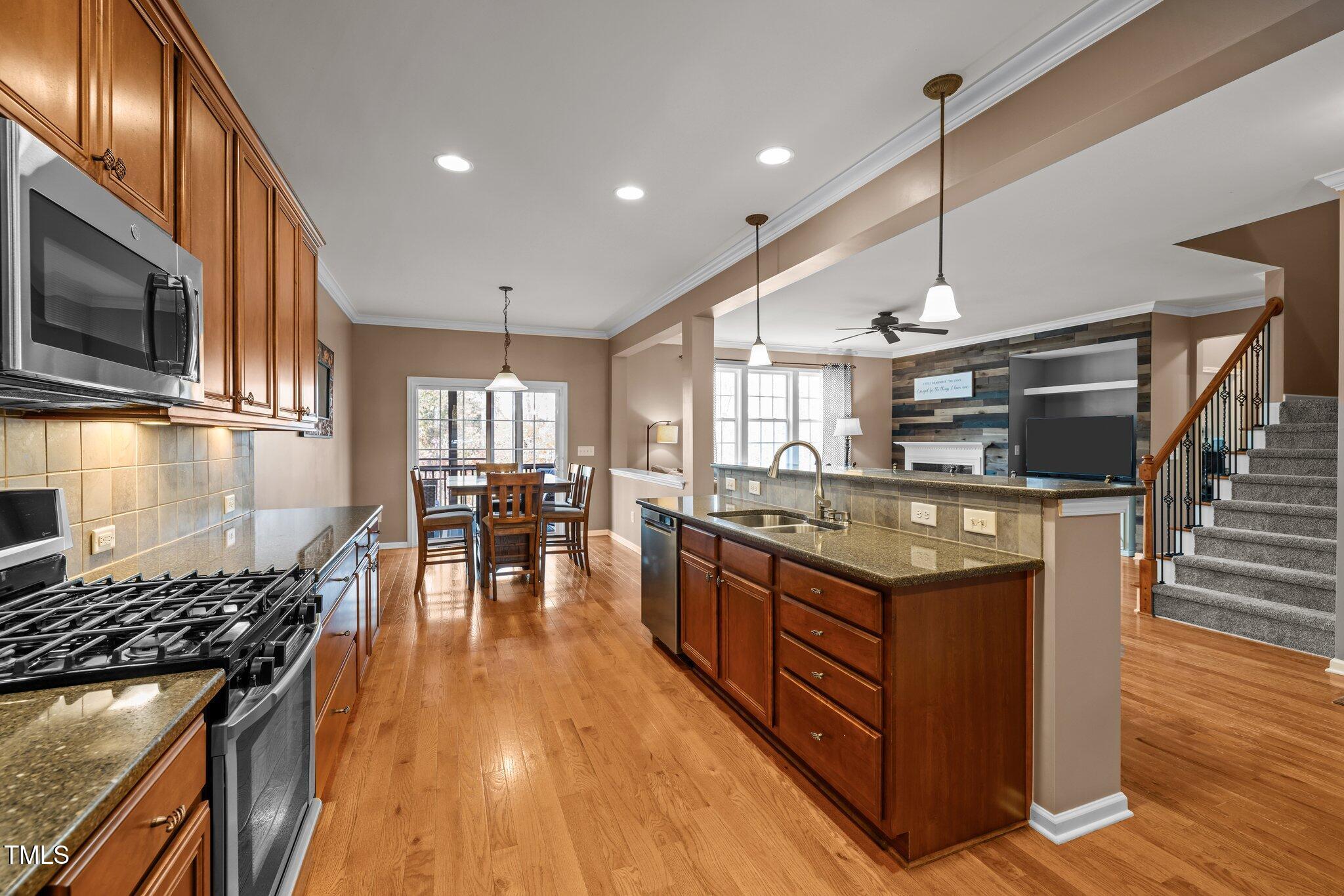Kitchen with a large granite island, gas range, wood cabinets, and open dining and living areas.
