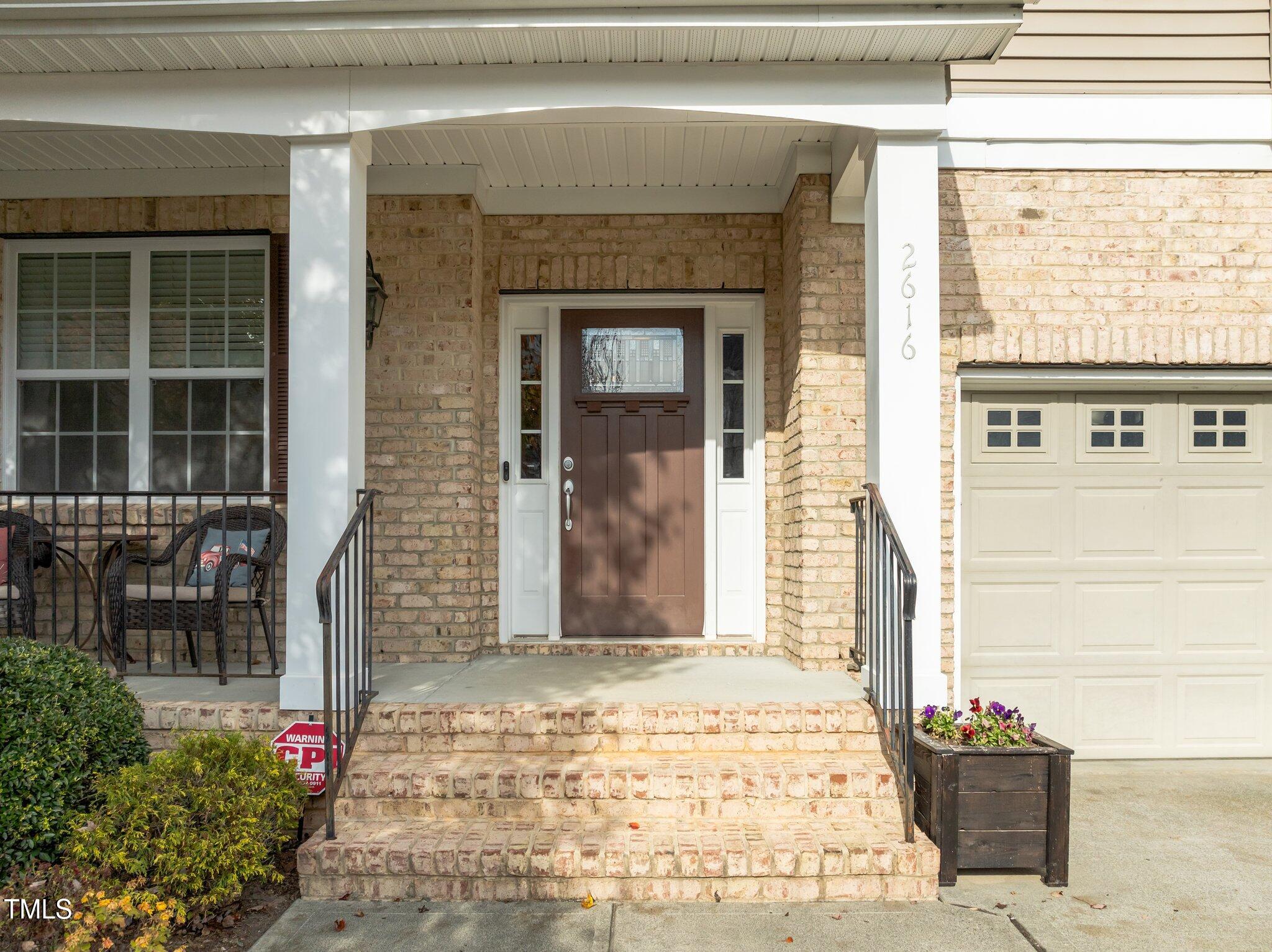 Brick home entrance with a brown door, covered porch, and brick steps.
