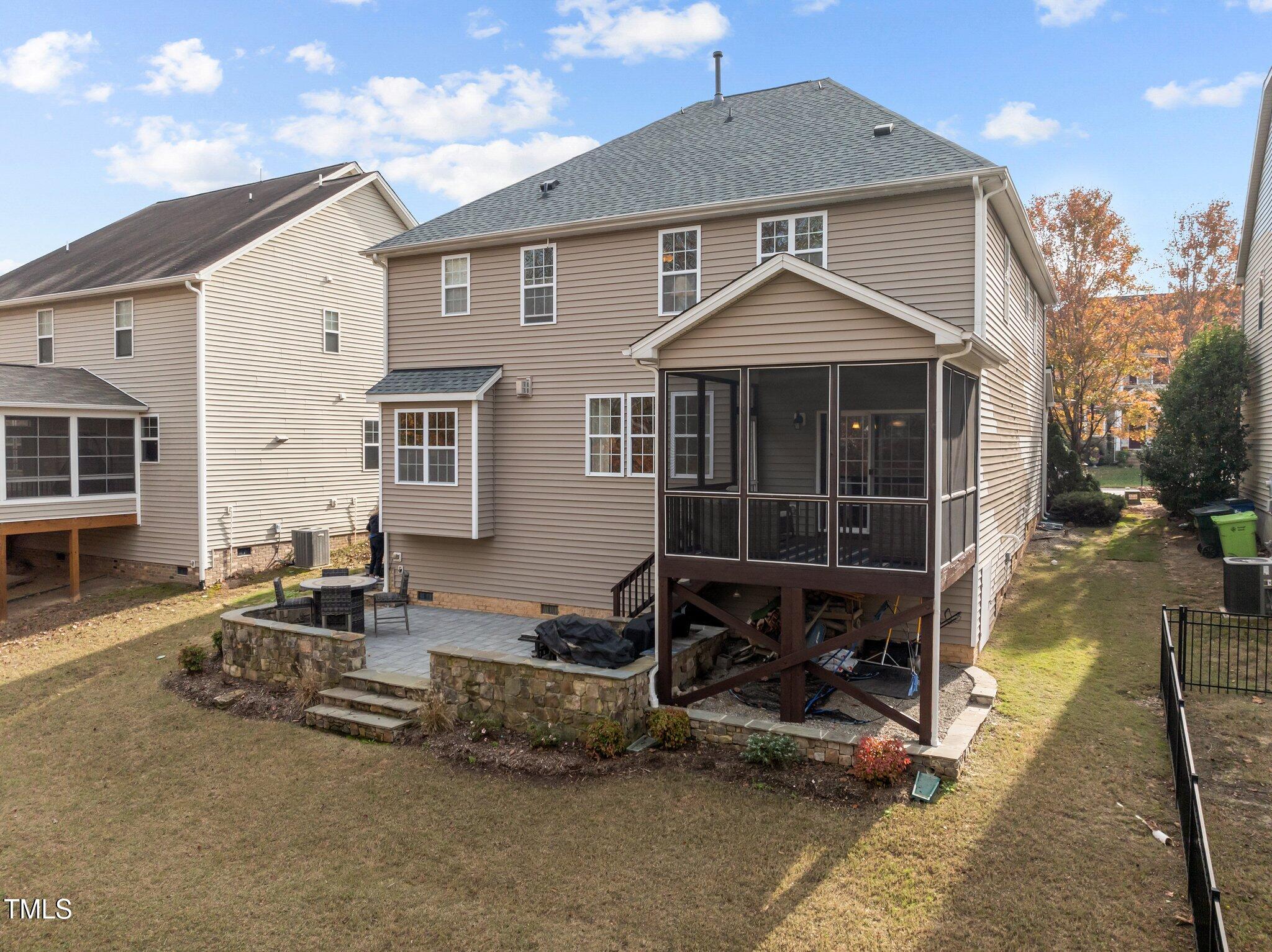 Home’s rear exterior with a raised screened porch and stone patio in the backyard.