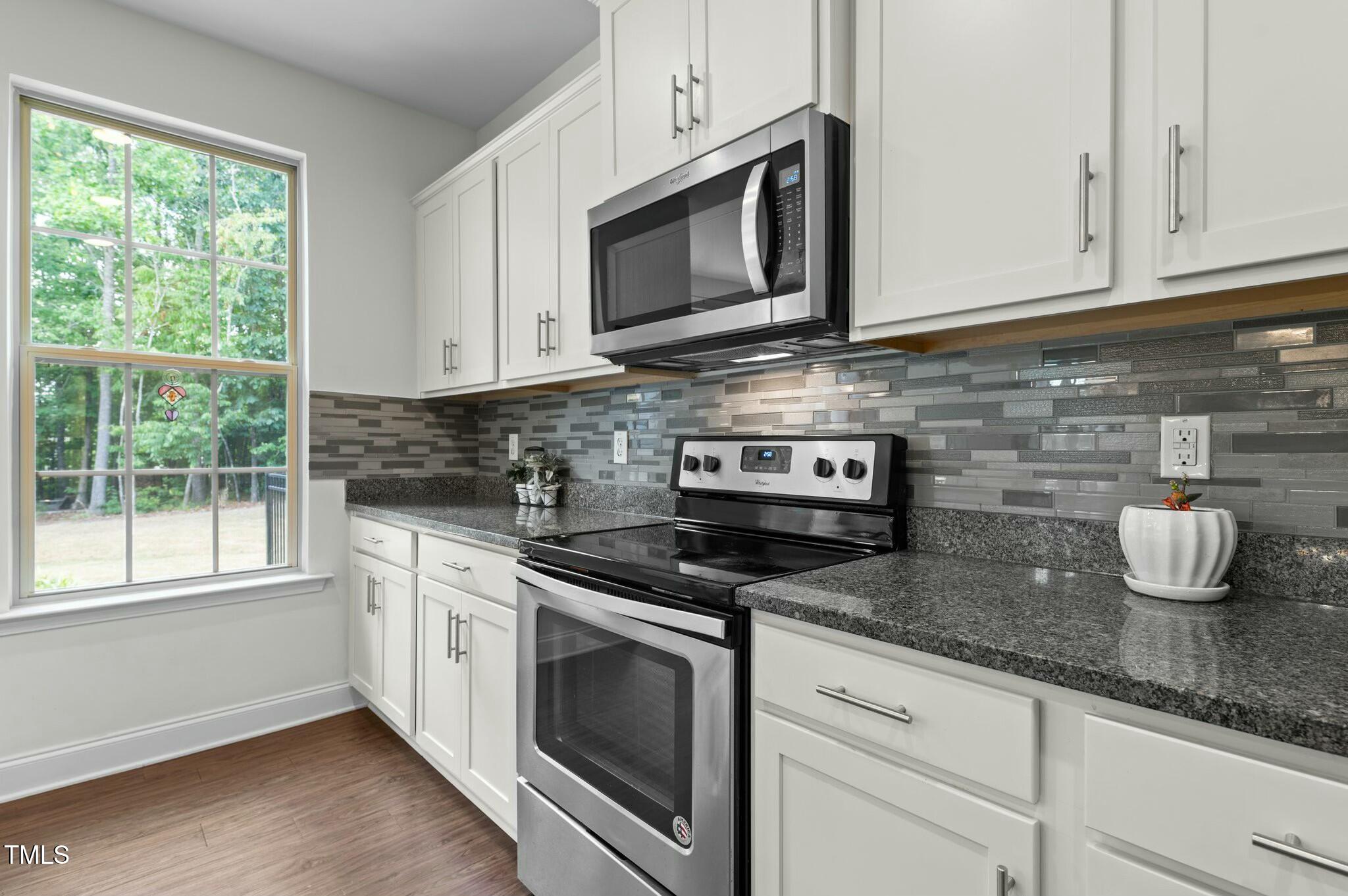 Kitchen with white cabinets, granite countertops, gray tile backsplash, and stainless steel appliances.