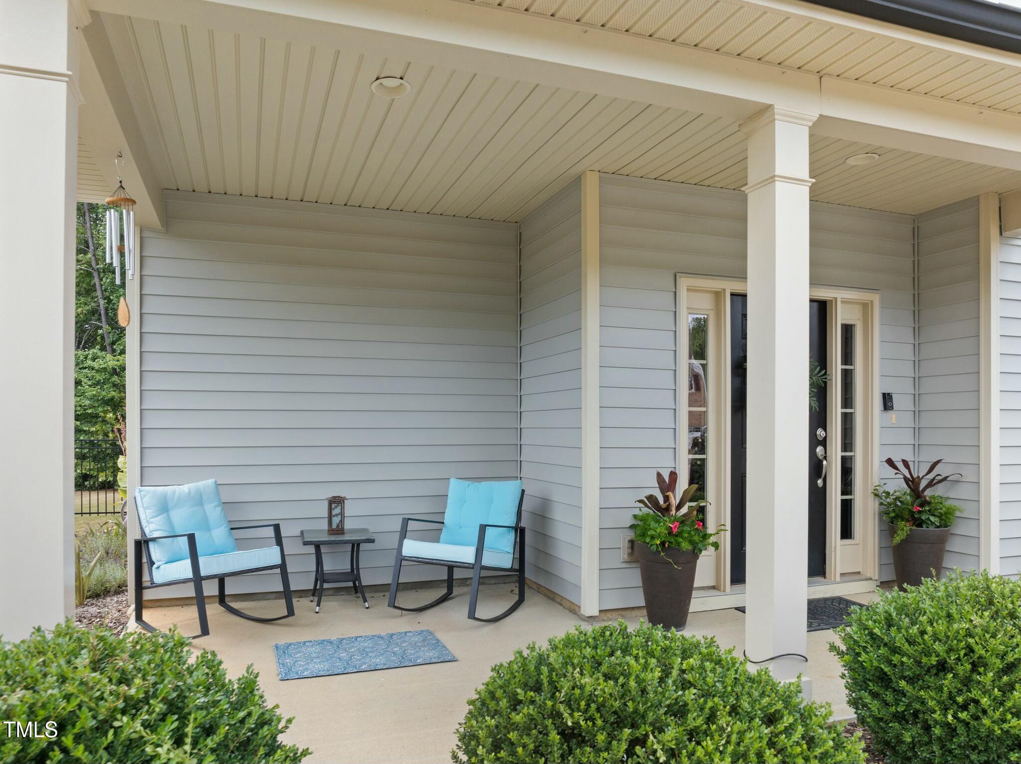 Covered front porch with blue-cushioned rocking chairs, gray siding, and potted plants.