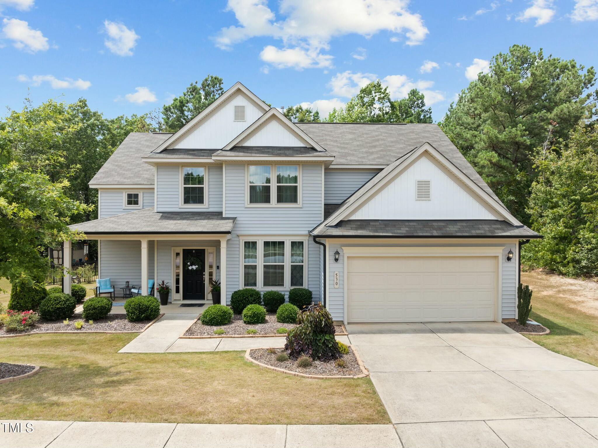 Two-story light blue home with a two-car garage, covered porch, and landscaped front yard.