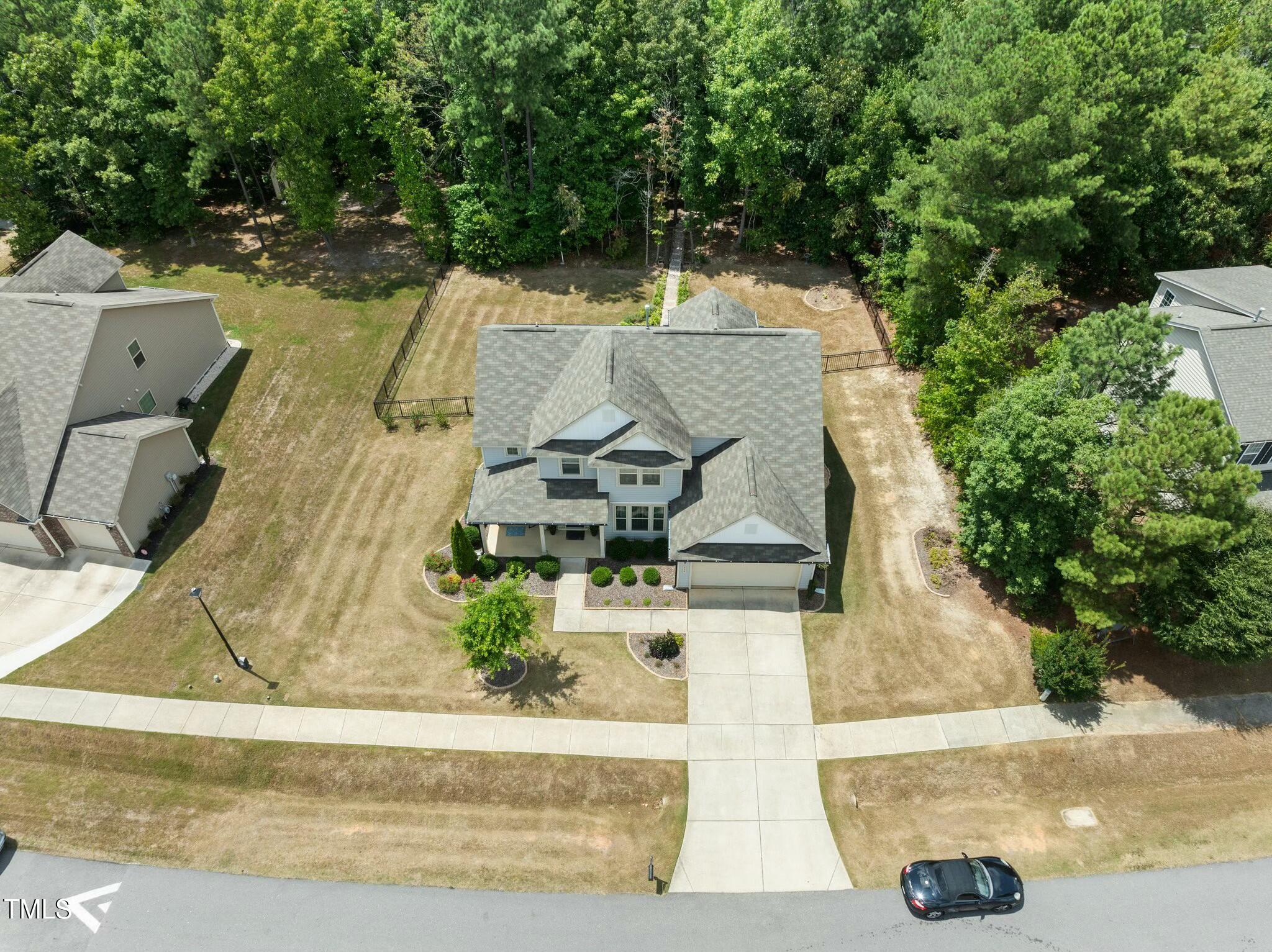 Aerial view of a two-story home with an attached garage and fenced, tree-lined backyard.