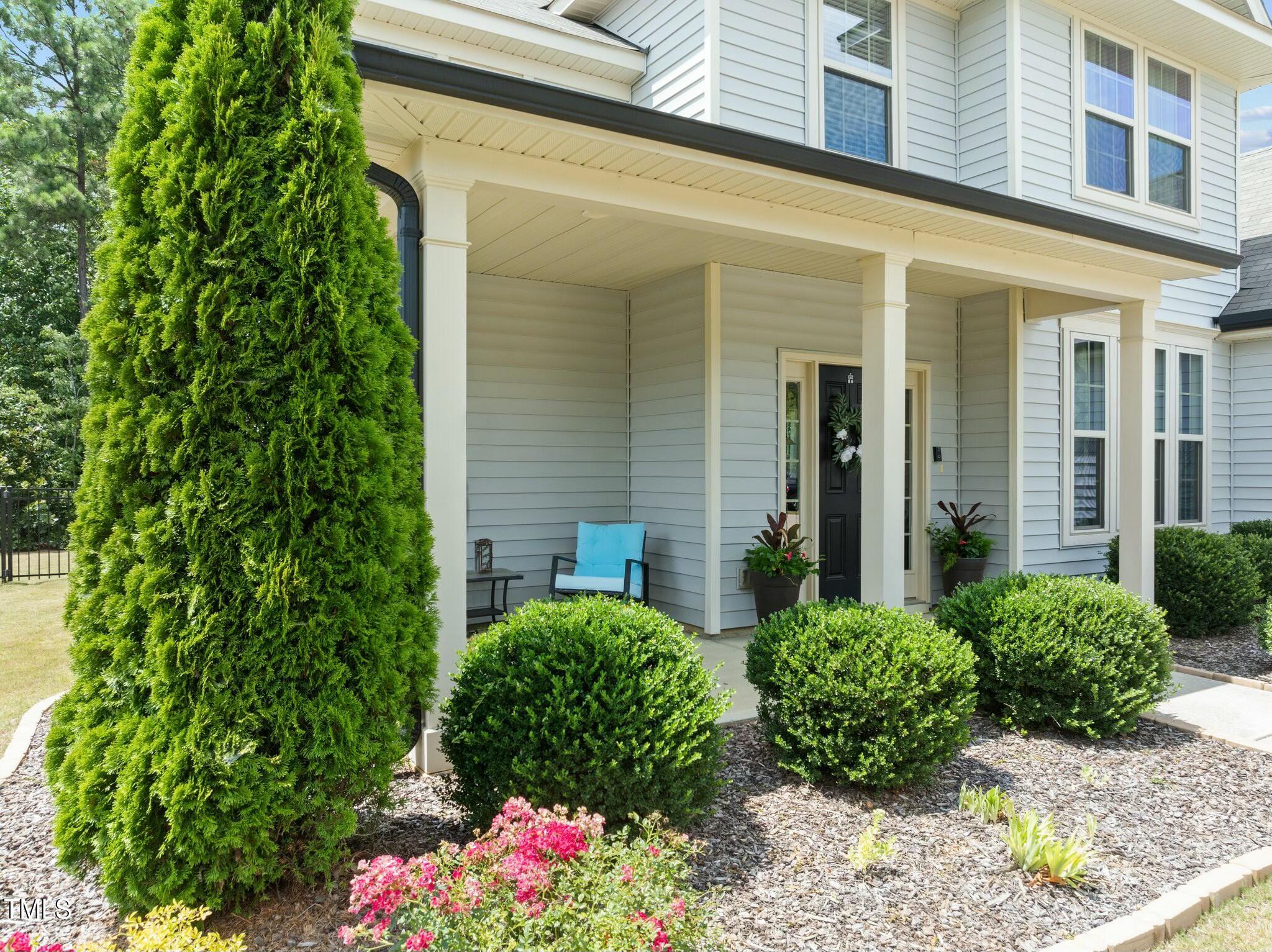 Two-story gray house with a covered porch, black front door, and lush landscaping.