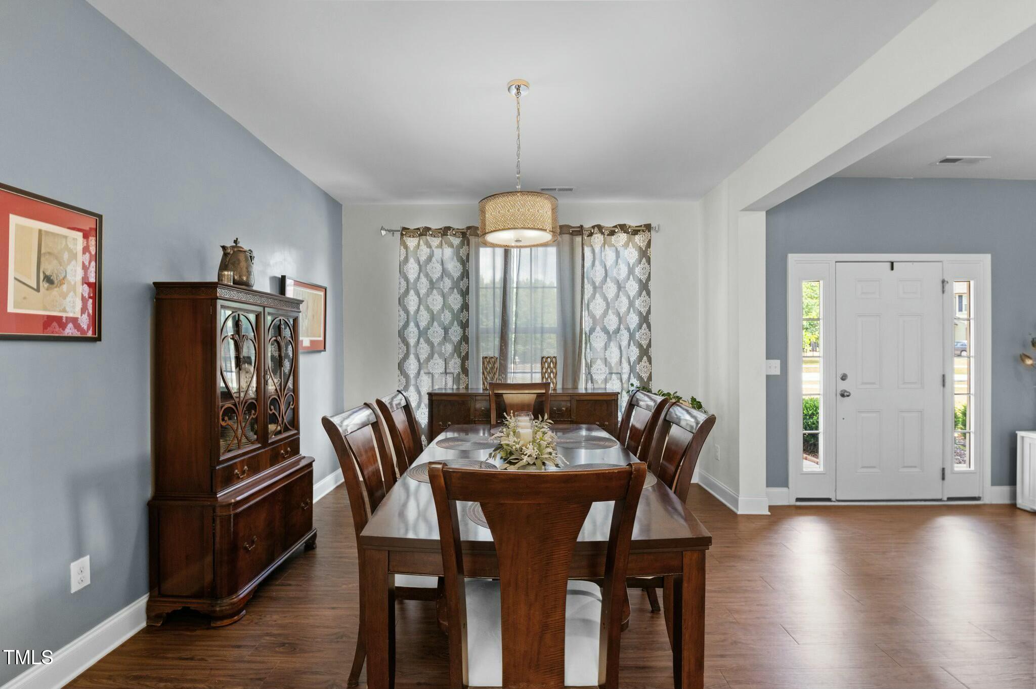 Dining room with a dark wood table, matching china cabinet, patterned curtains, and blue-gray walls.