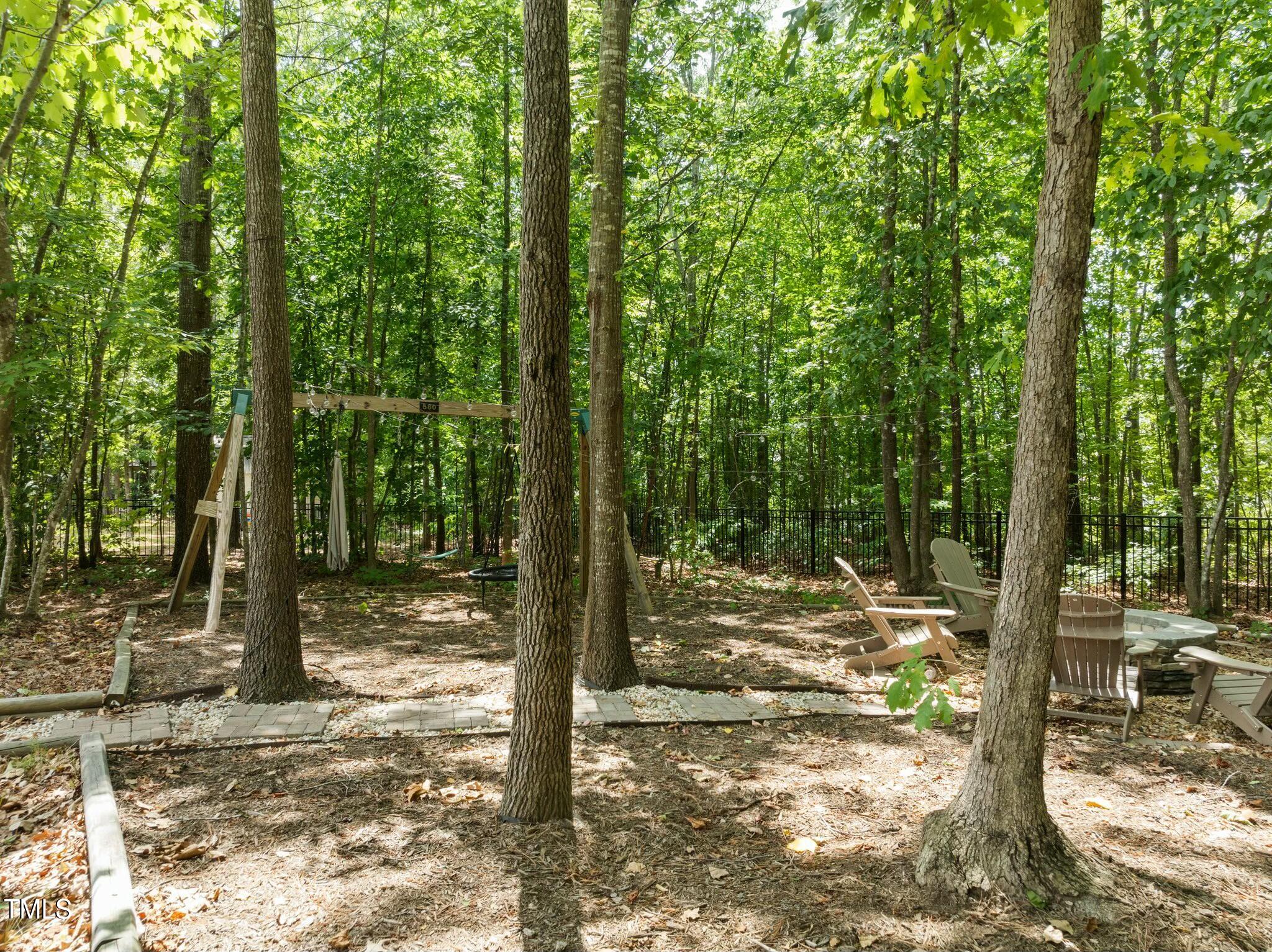 Wooded backyard with a swing set, Adirondack chairs, and a fire pit.