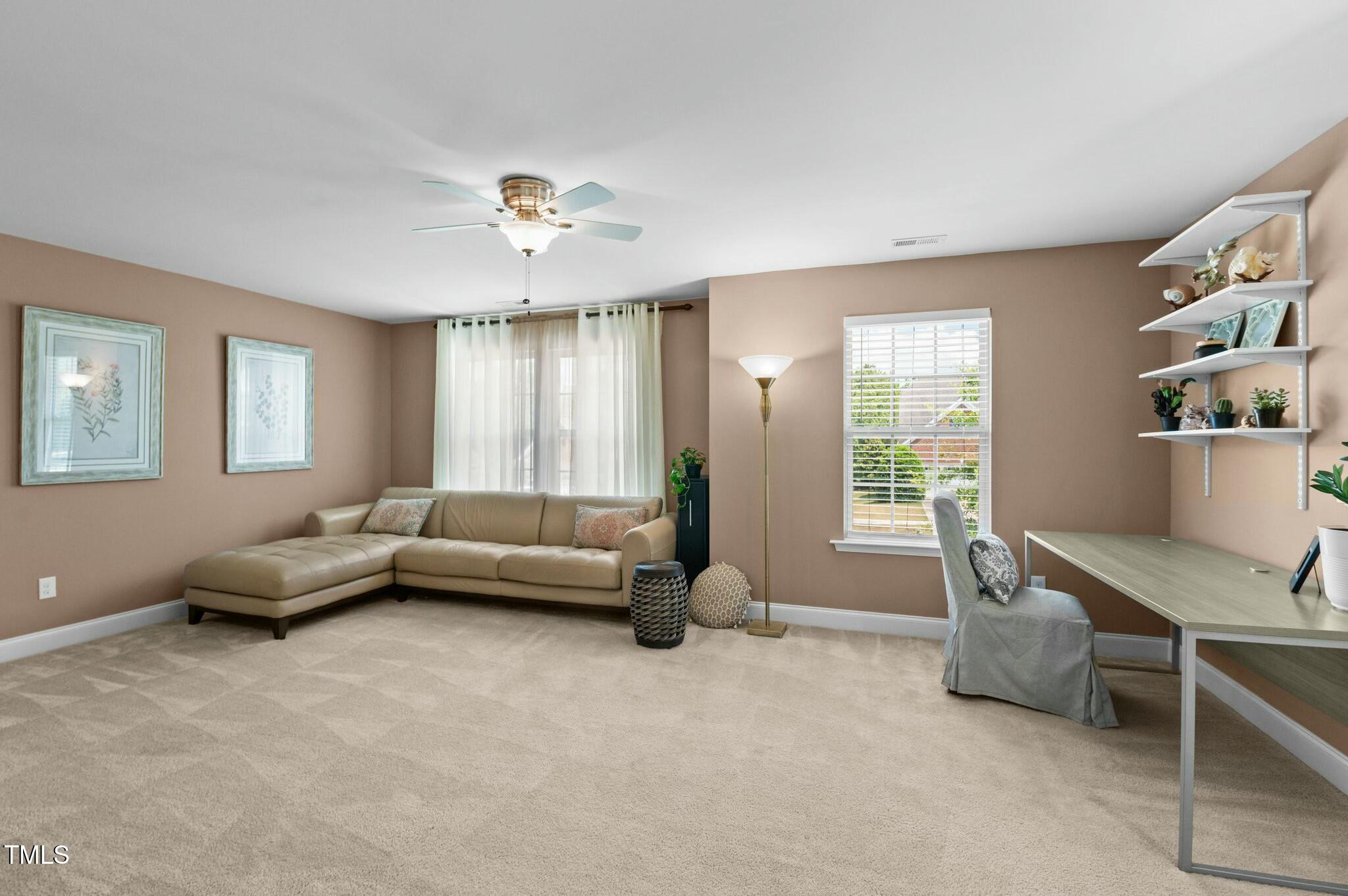 Staged living room with a beige sectional, carpet, and a desk beside a window.