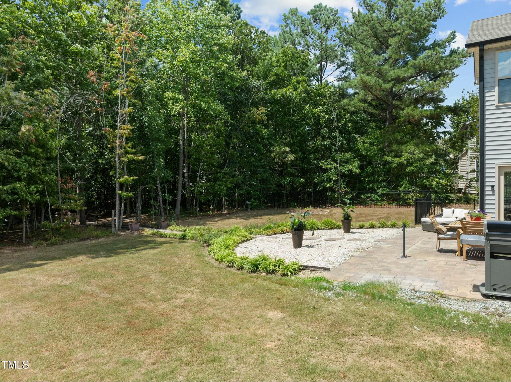 Backyard with mature trees, a white-stone garden bed, and a paved patio with outdoor seating.