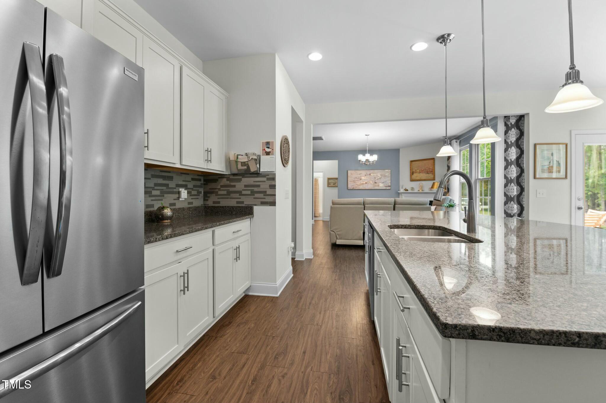 Modern kitchen with a granite island and sink opening into a furnished living room.