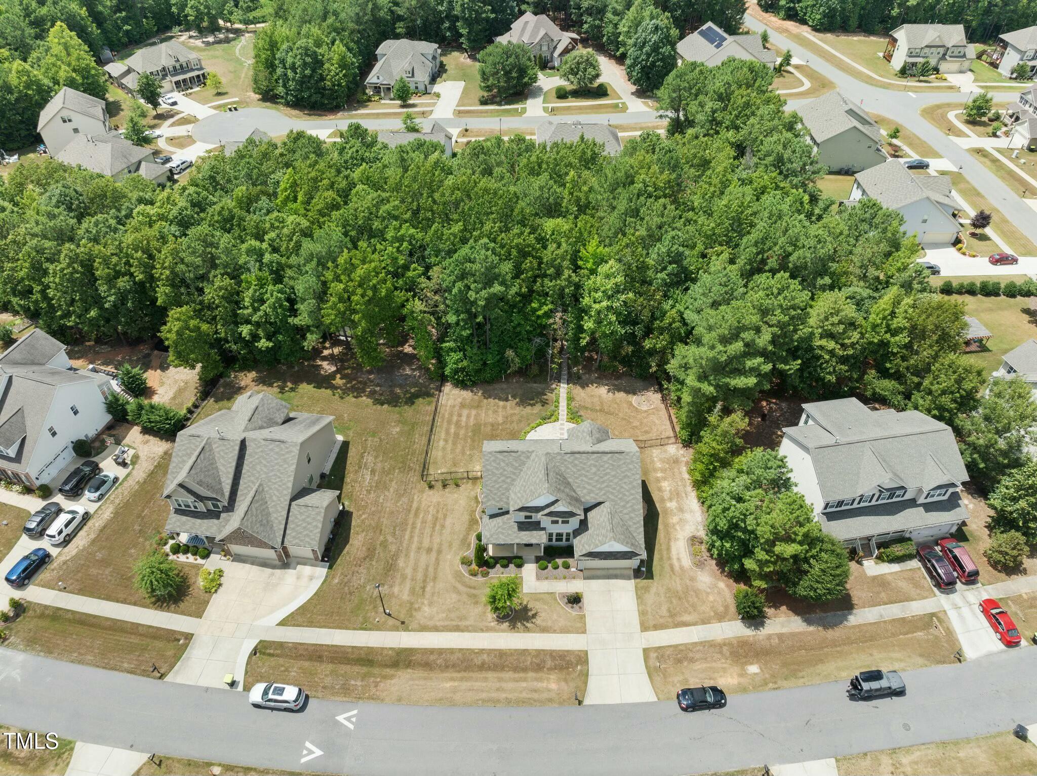 Aerial view of a two-story home with a tree-lined backyard and neighboring houses.