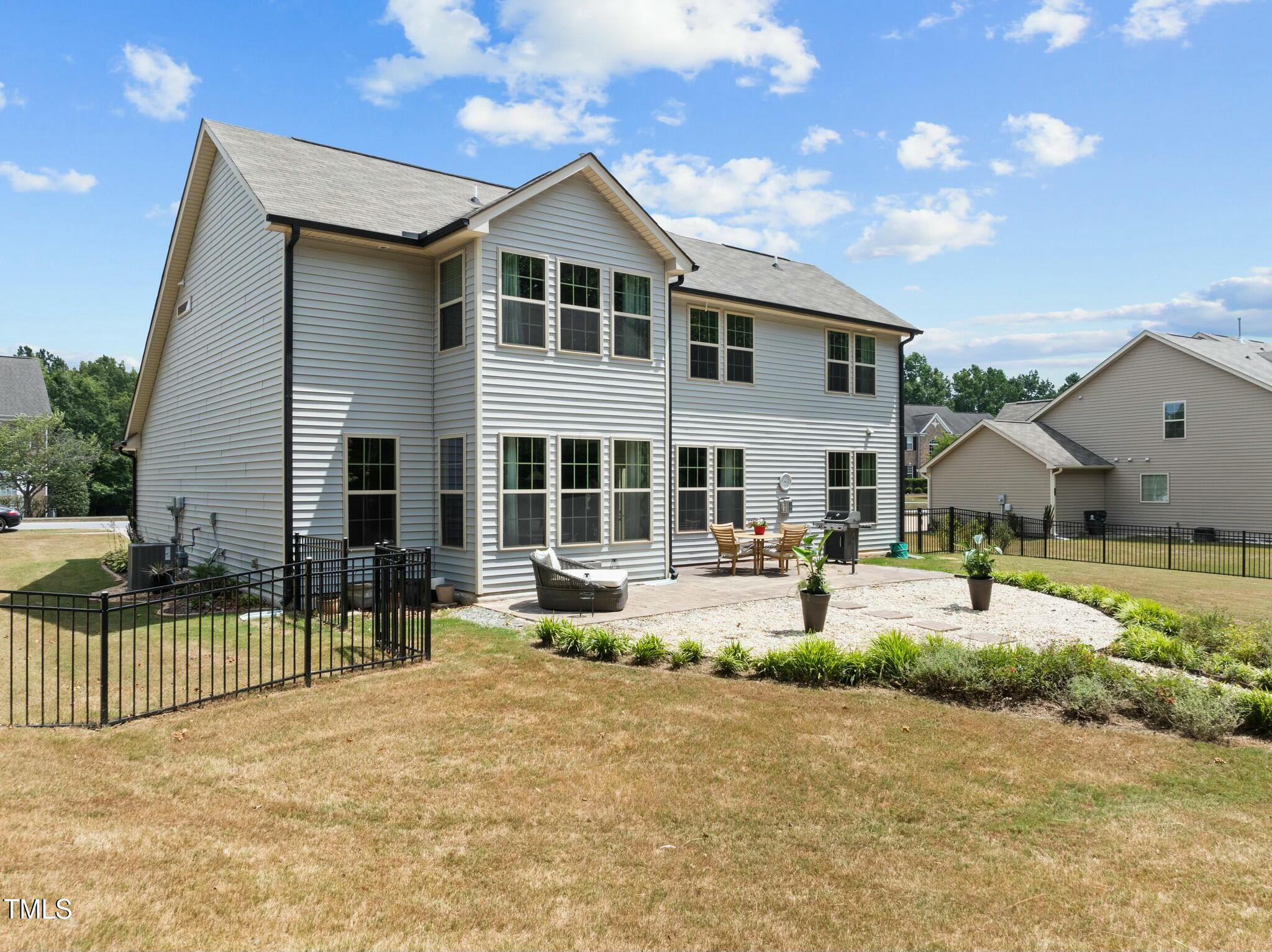 Rear of a two-story gray-sided home with a fenced yard and patio seating.