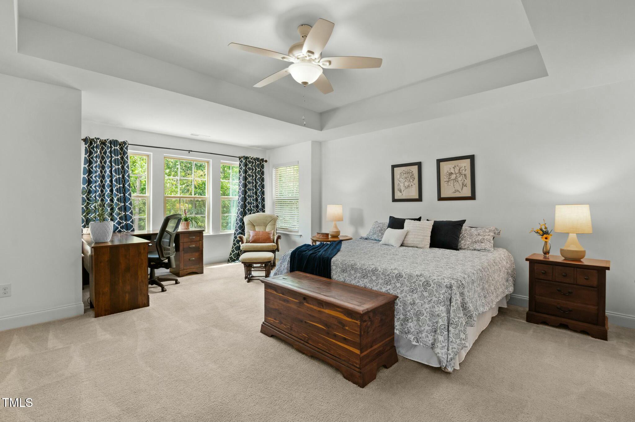 Furnished bedroom with a large patterned bed, wooden chest, desk, and windows with blue curtains.