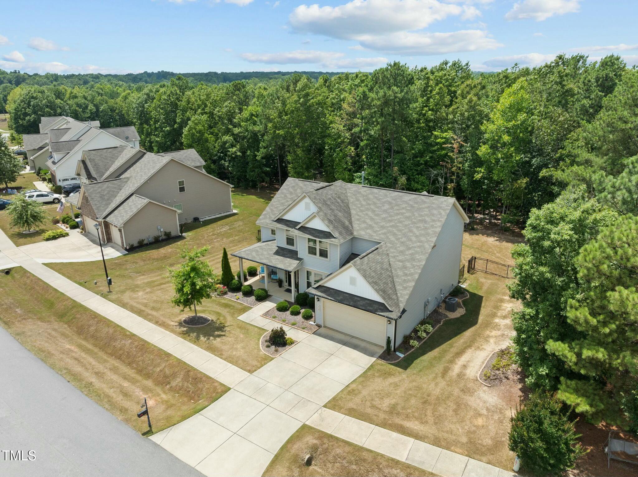 Aerial view of a two-story home with an attached garage, driveway, and wooded surroundings.