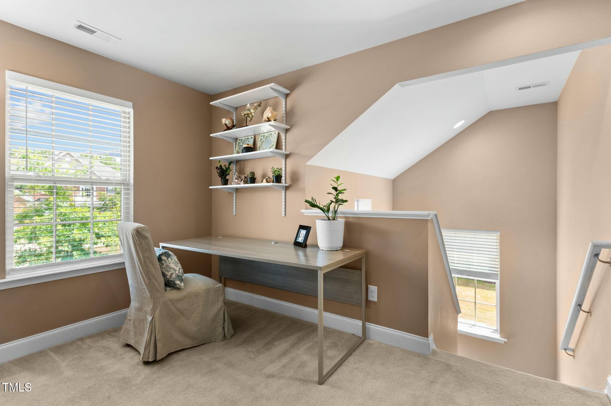 Upstairs office with a desk beneath wall shelves, beside a large window and open stairwell.