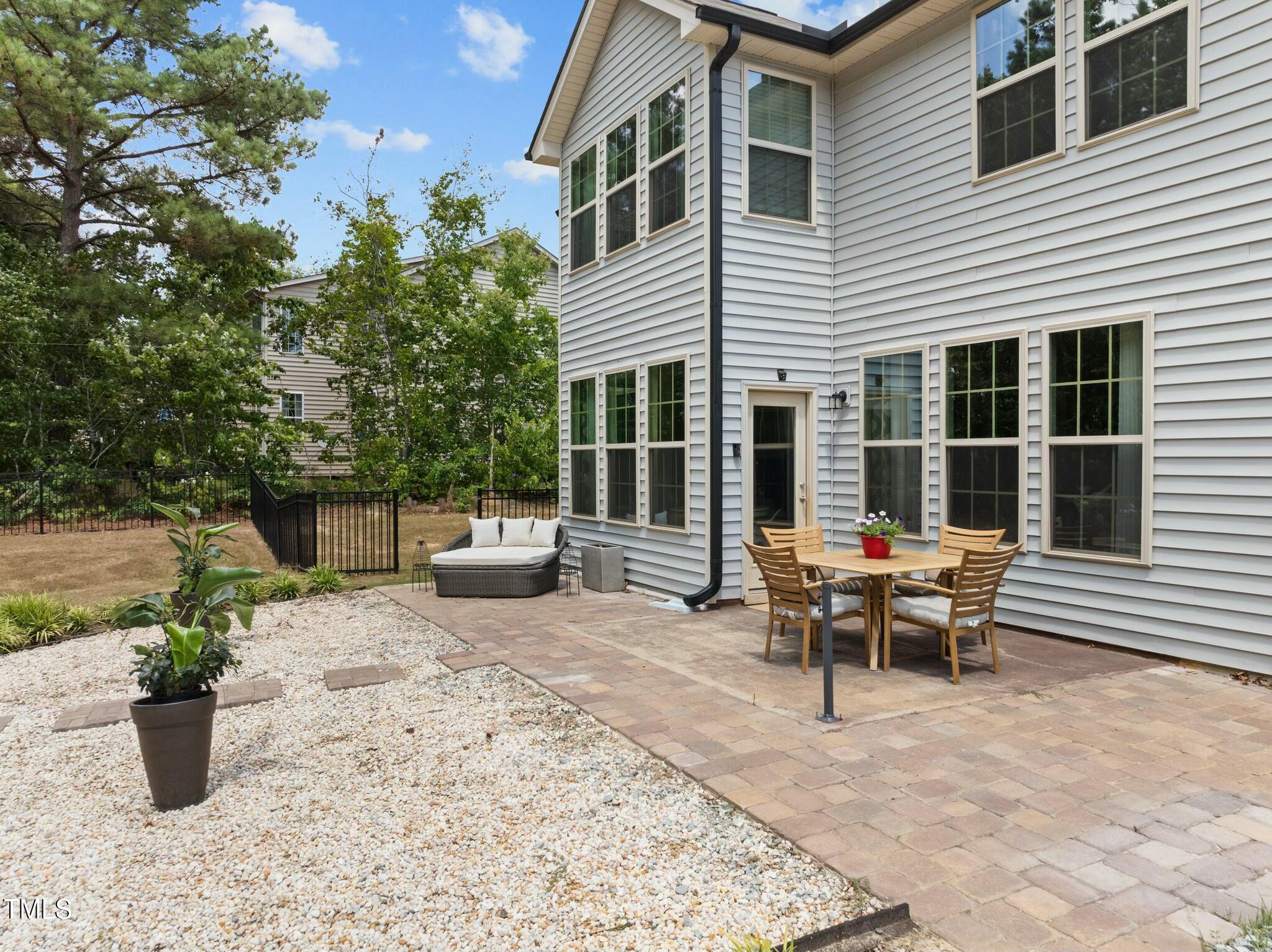Rear patio with outdoor dining set and cushioned loveseat beside a two-story home.