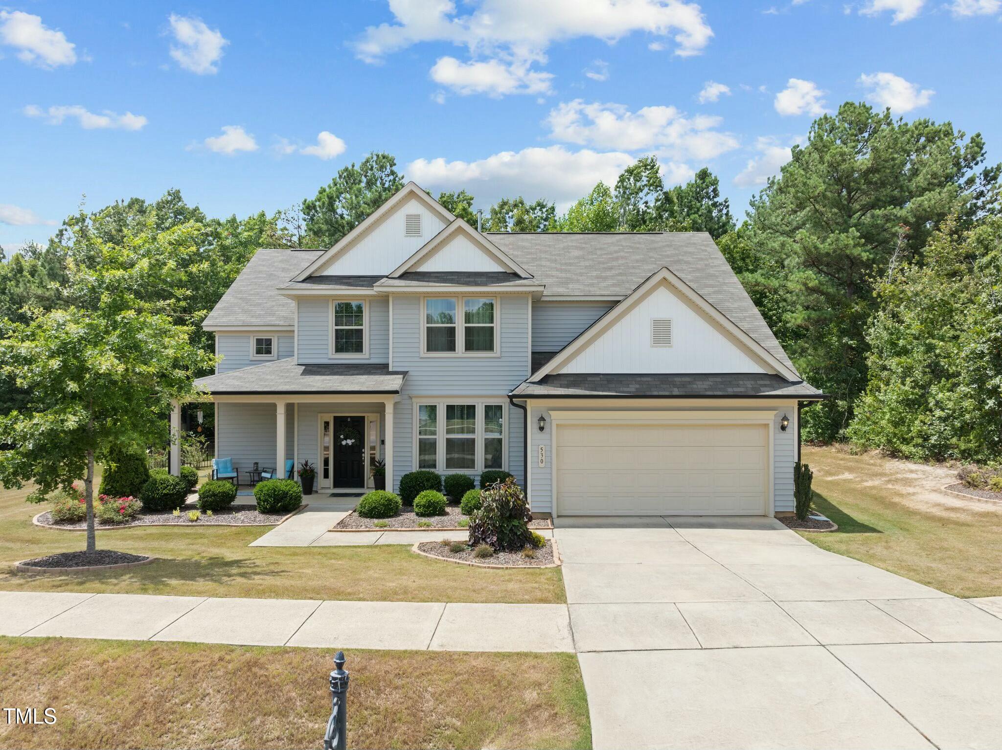 Two-story gray house with a two-car garage, covered porch, and landscaped front yard.