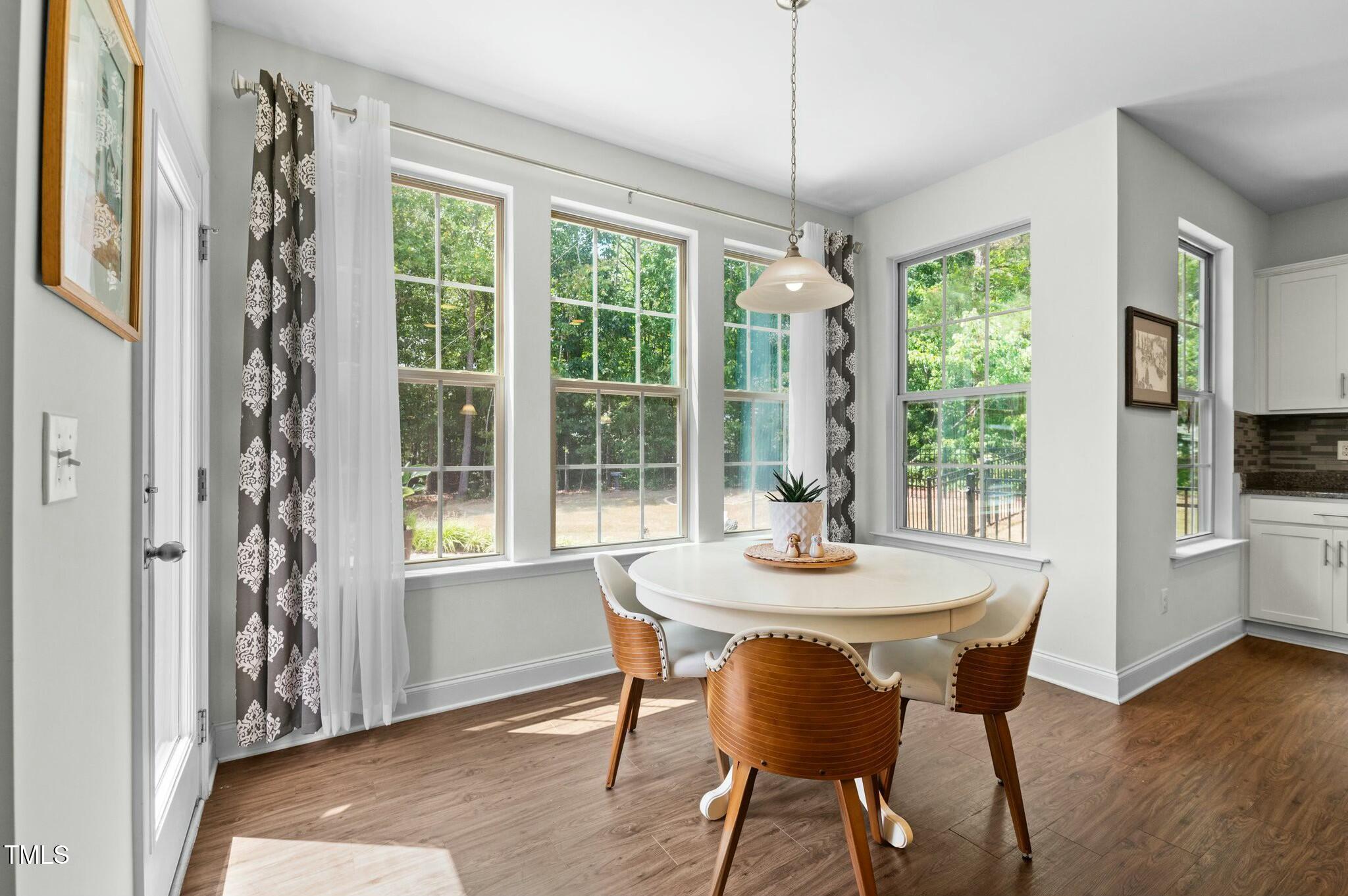 Dining area with an oval table, wood-backed chairs, and large windows overlooking a fenced pool.