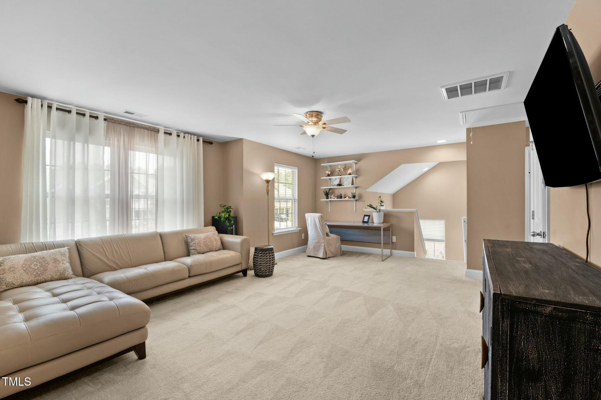 Upstairs living area with a tan sectional, beige carpet, ceiling fan, and desk beside the stair opening.