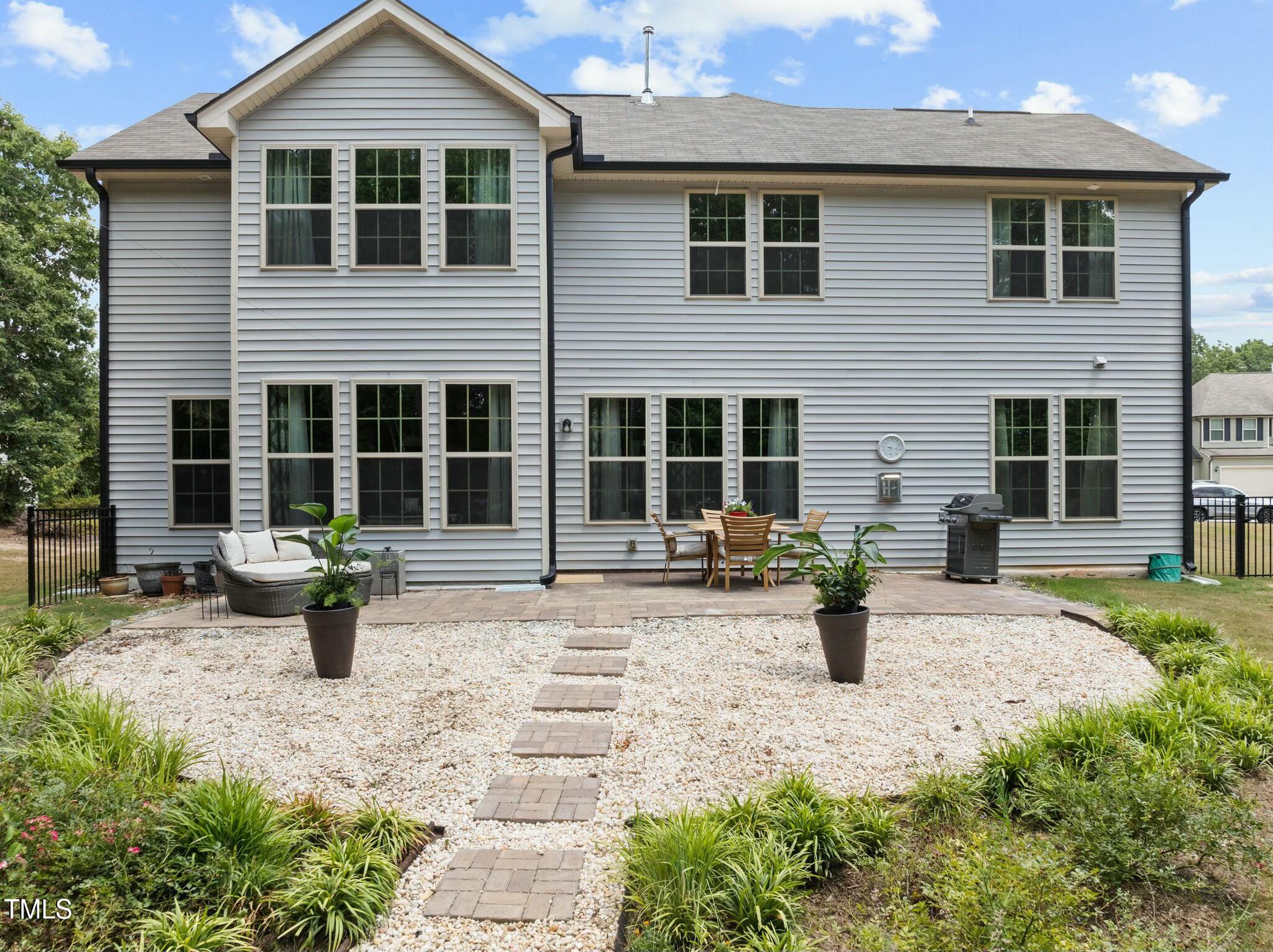 Rear of a two-story gray house with a gravel path leading to a furnished patio.
