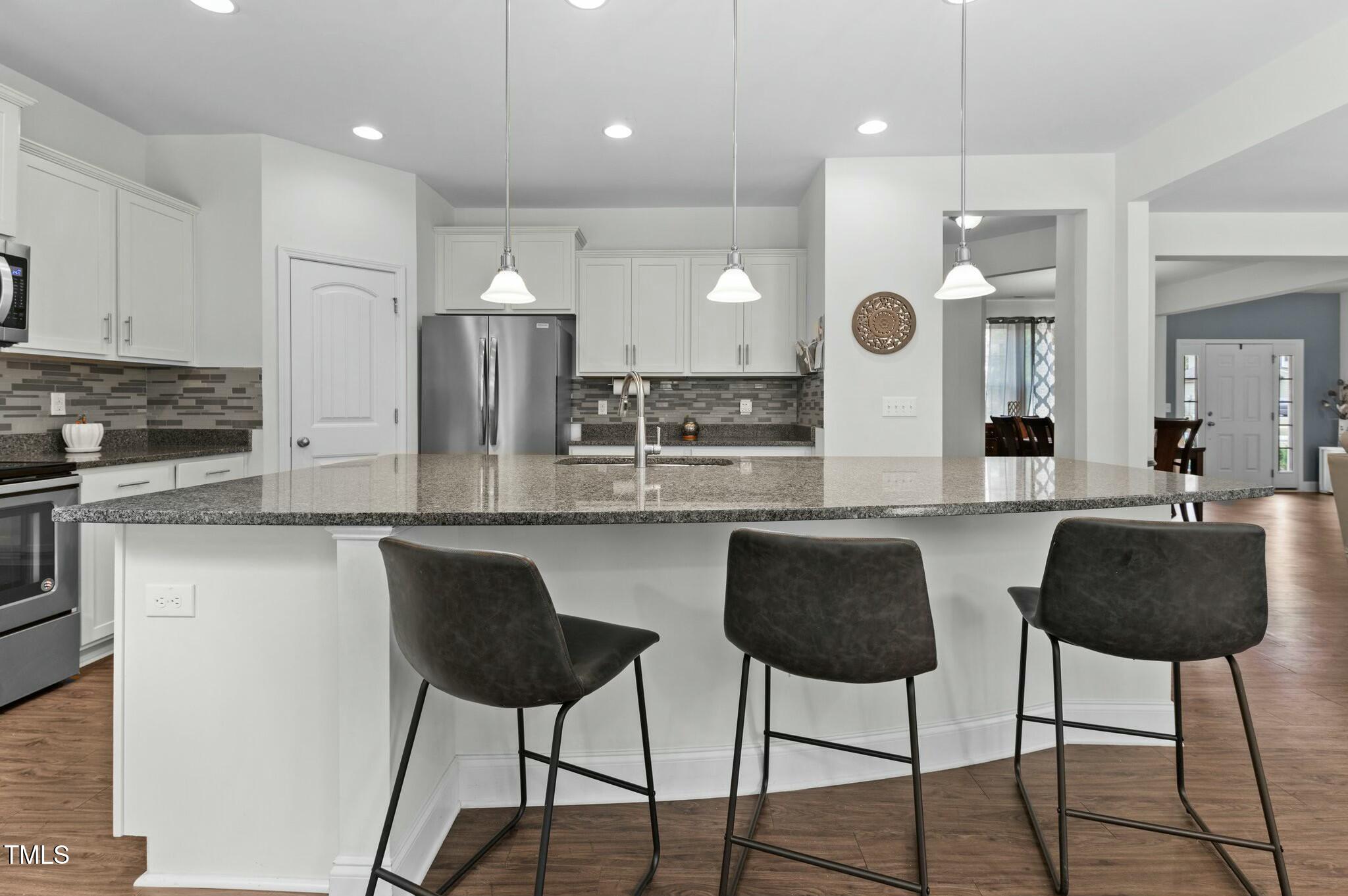 Kitchen with white cabinets, stainless steel appliances, and a granite island with three bar stools.
