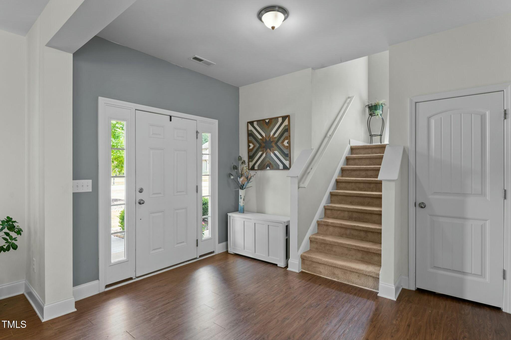Entry foyer with a white front door, carpeted staircase, and dark wood flooring.