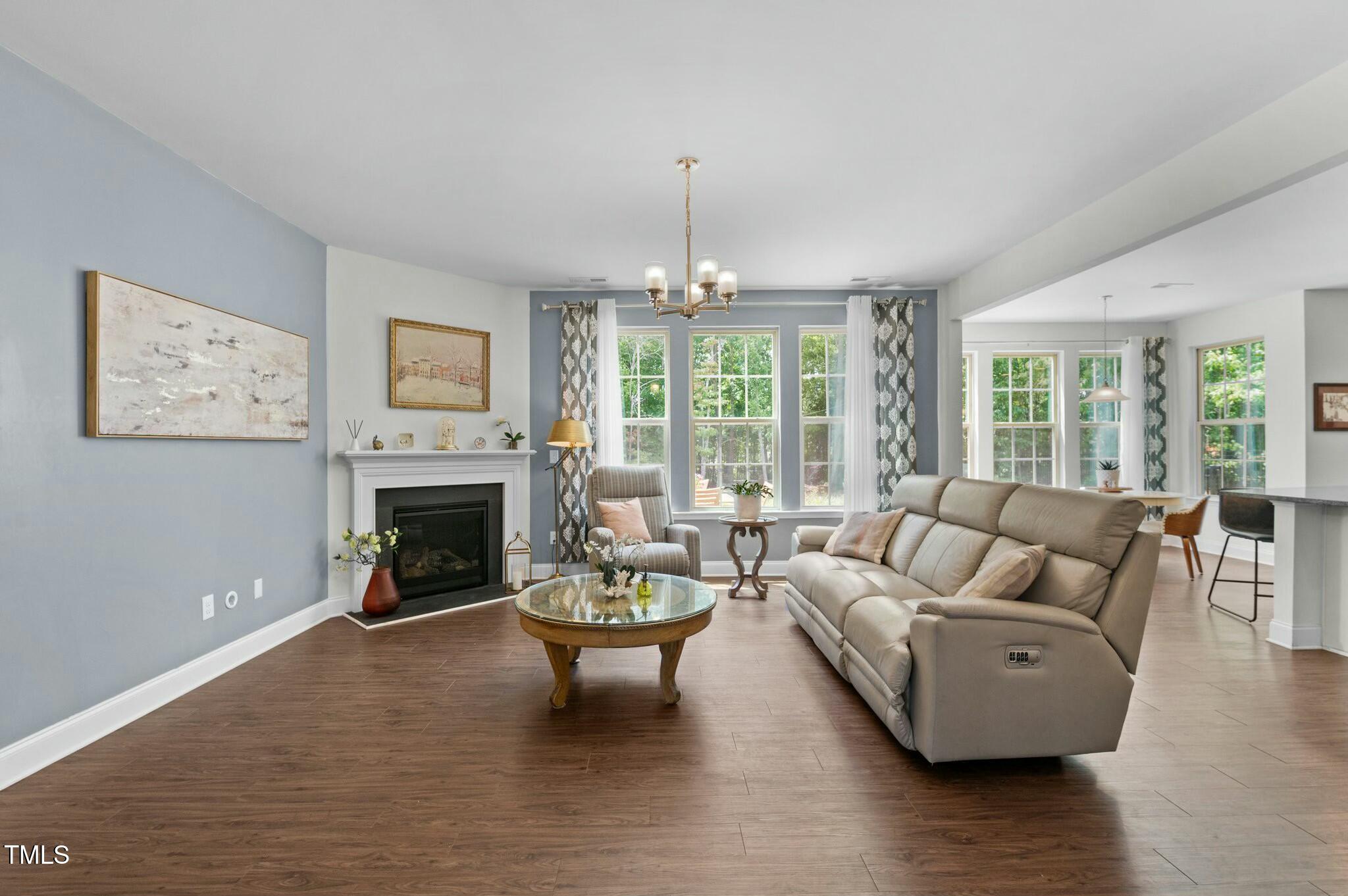 Furnished living room with a fireplace, beige reclining sofa, and large windows.